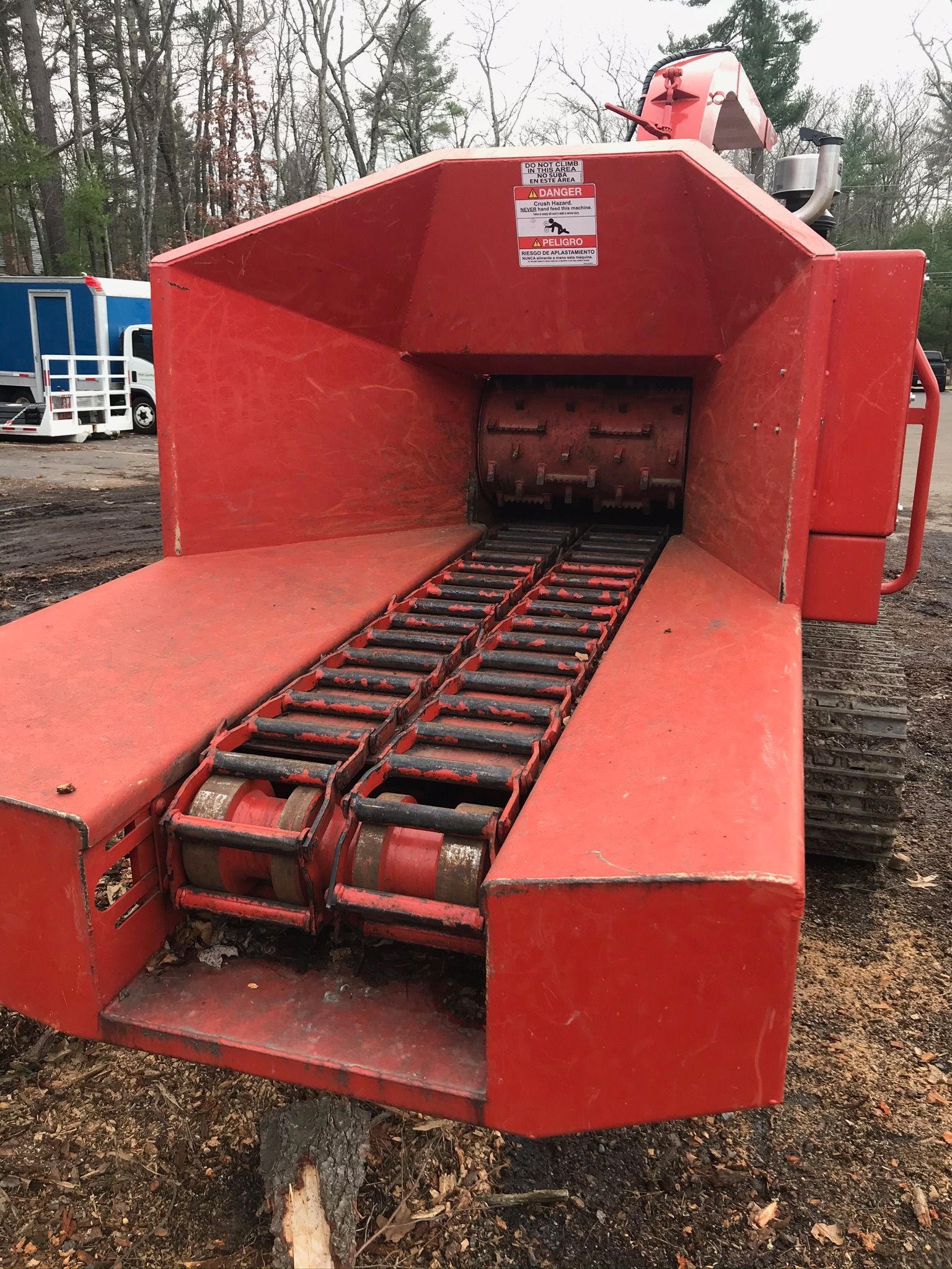 Red industrial wood chipper with conveyor and chute, parked outdoors on a dirt lot