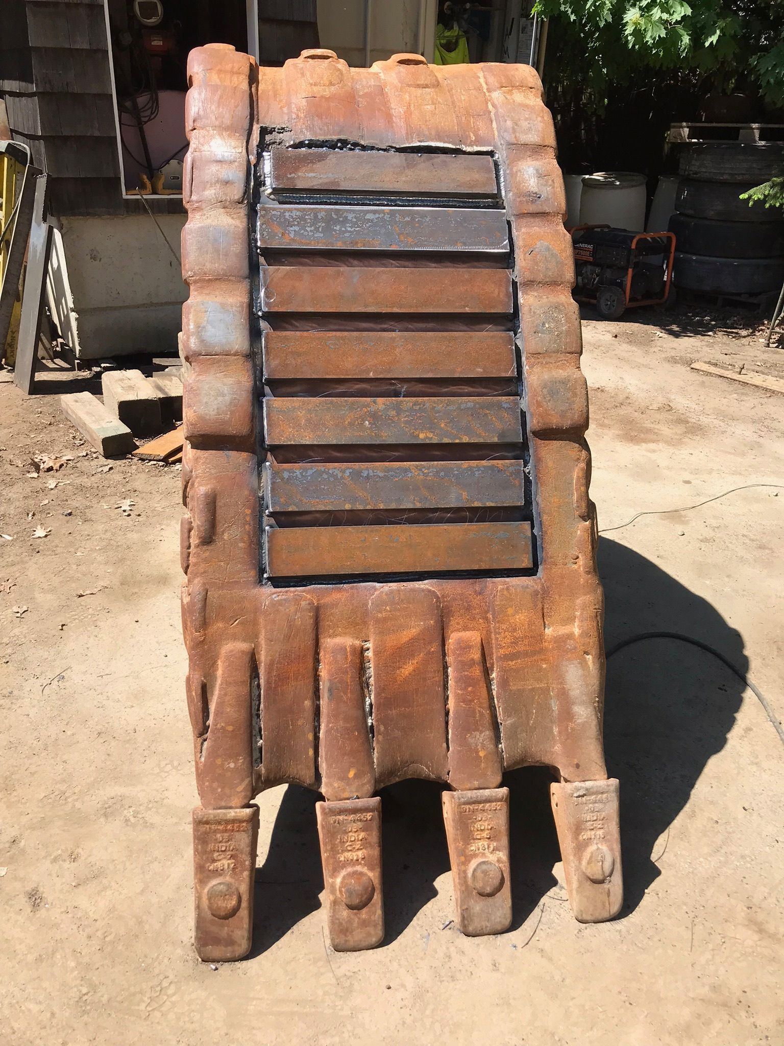 Rusty metal robot hand sculpture with segmented fingers and a dark central panel outdoors.