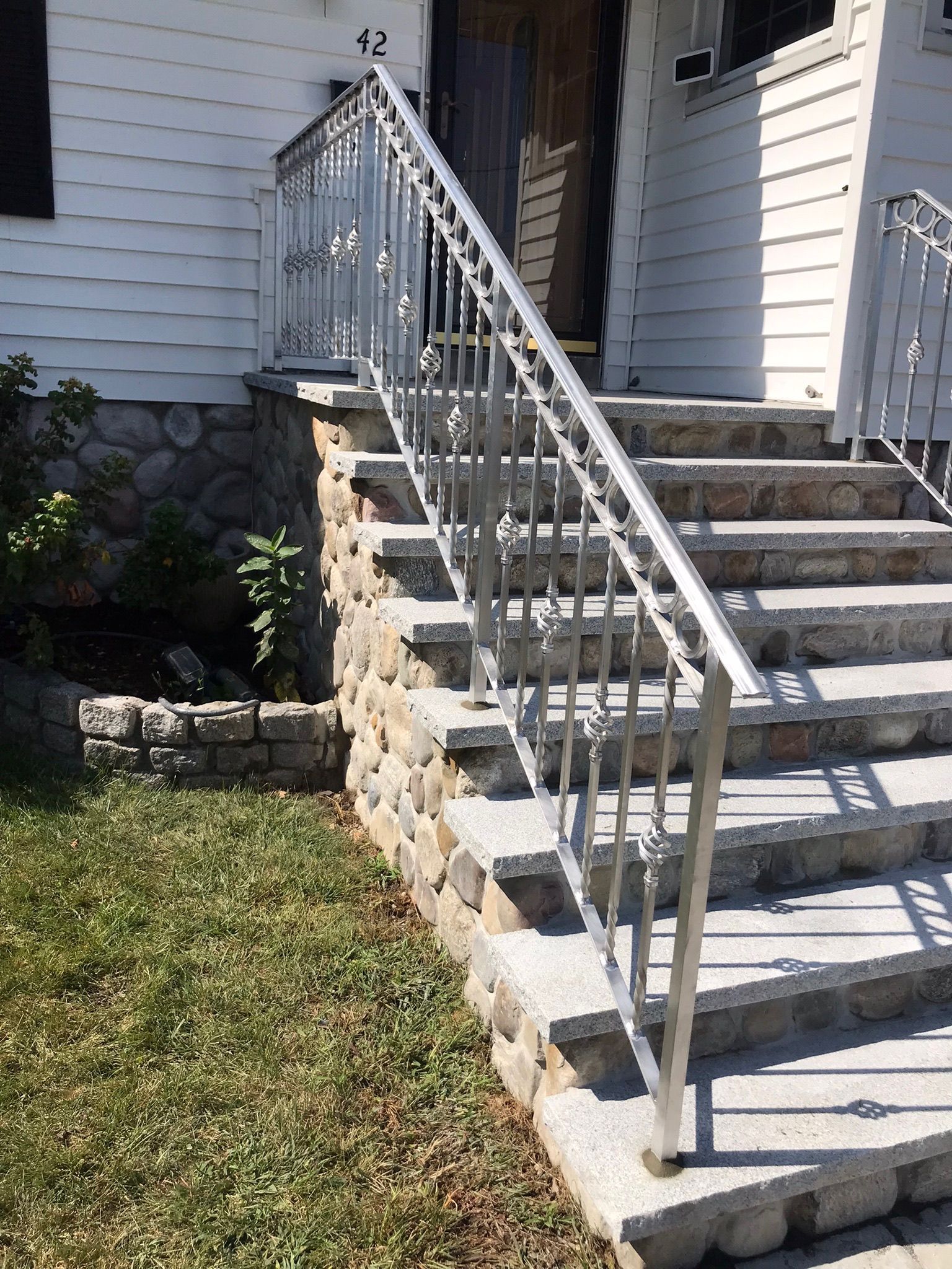 Front steps to a house with gray stone stairs and white metal railings leading to the front door.
