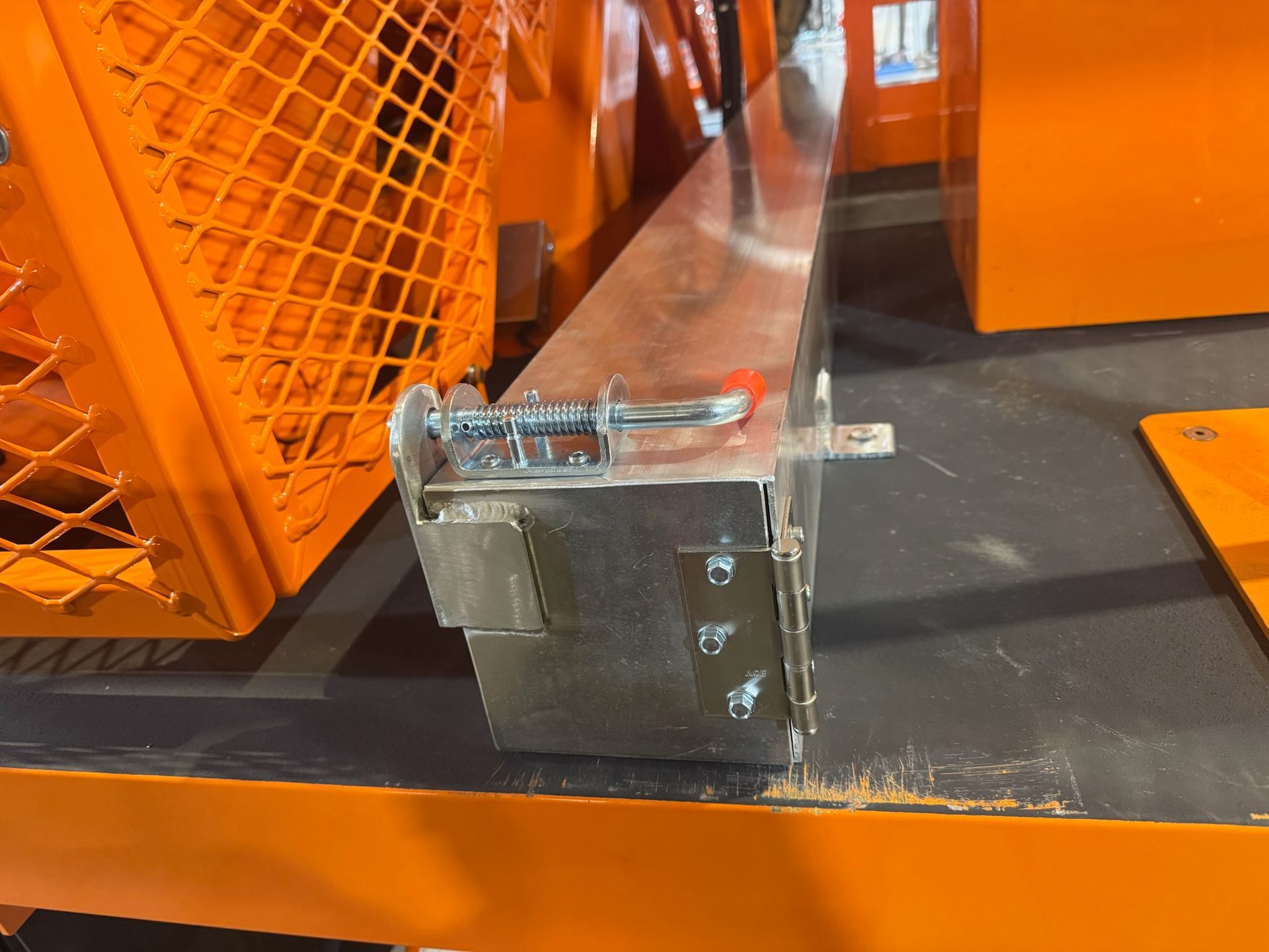 Orange industrial machinery with a clear protective guard and metal bracket on a black surface