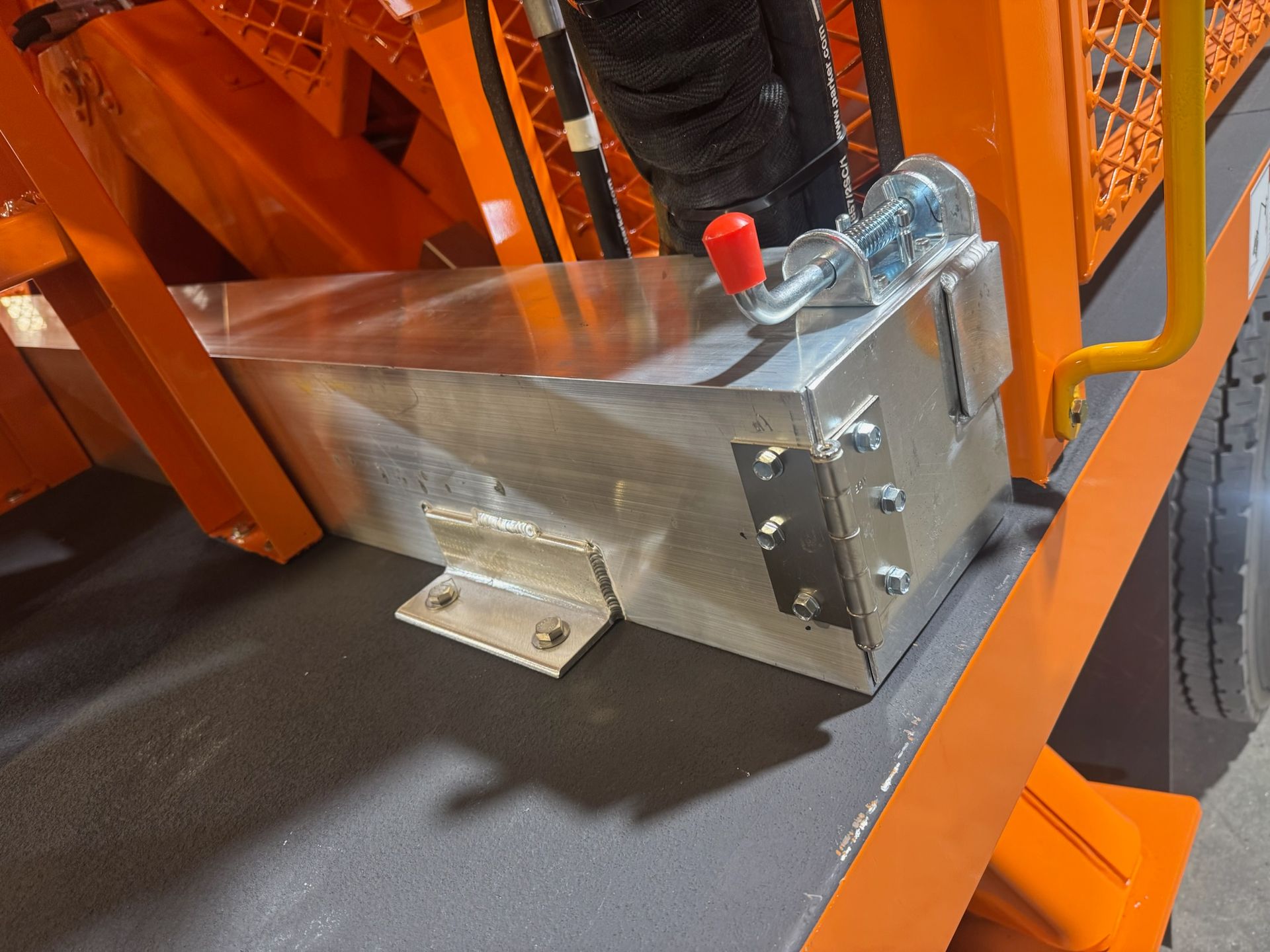 Metal box mounted on an orange industrial frame, with a red-capped fitting and wheels nearby