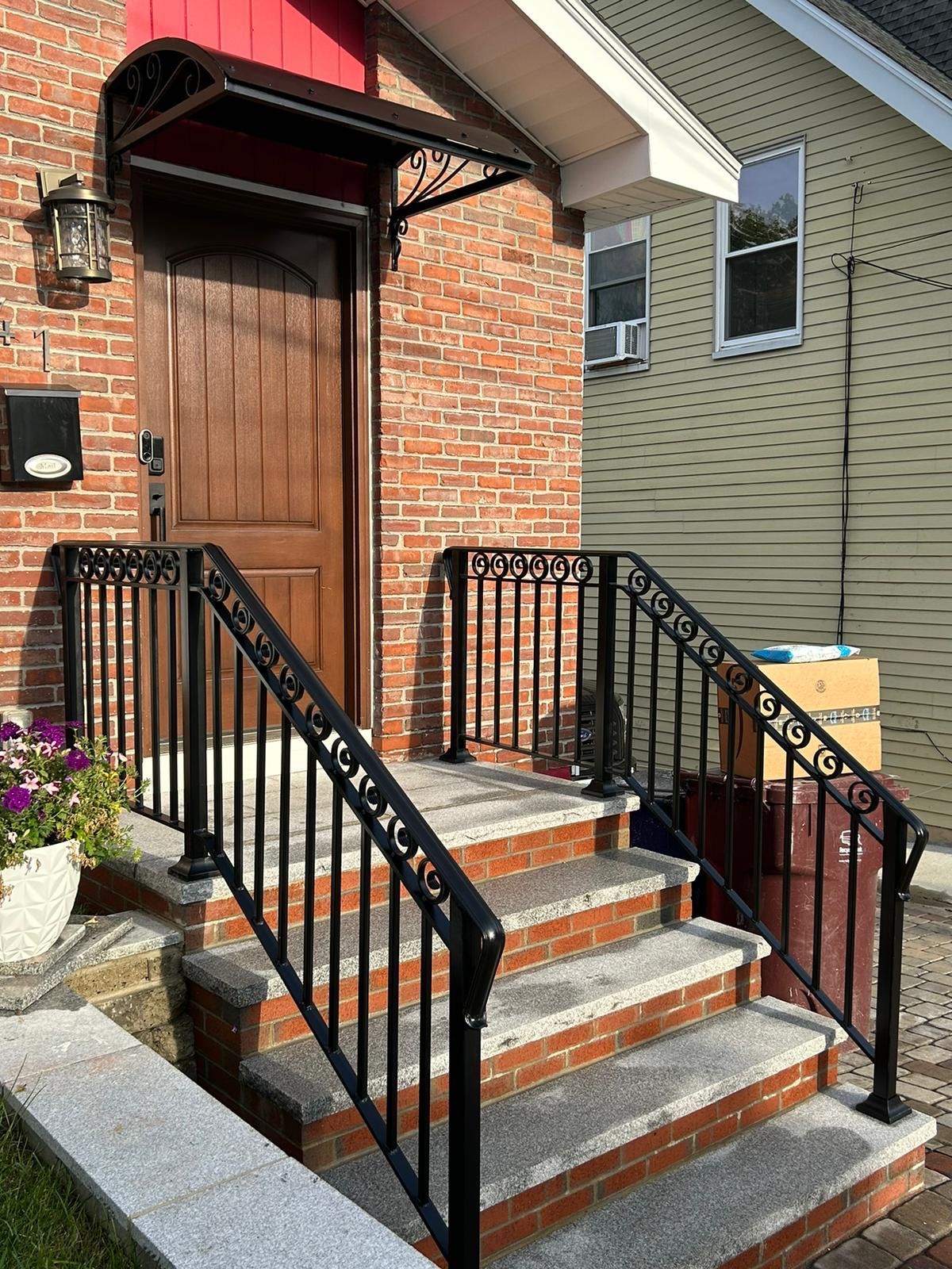 Brick house front steps with black railings, red-brick stoop, and a wooden door under a small awning