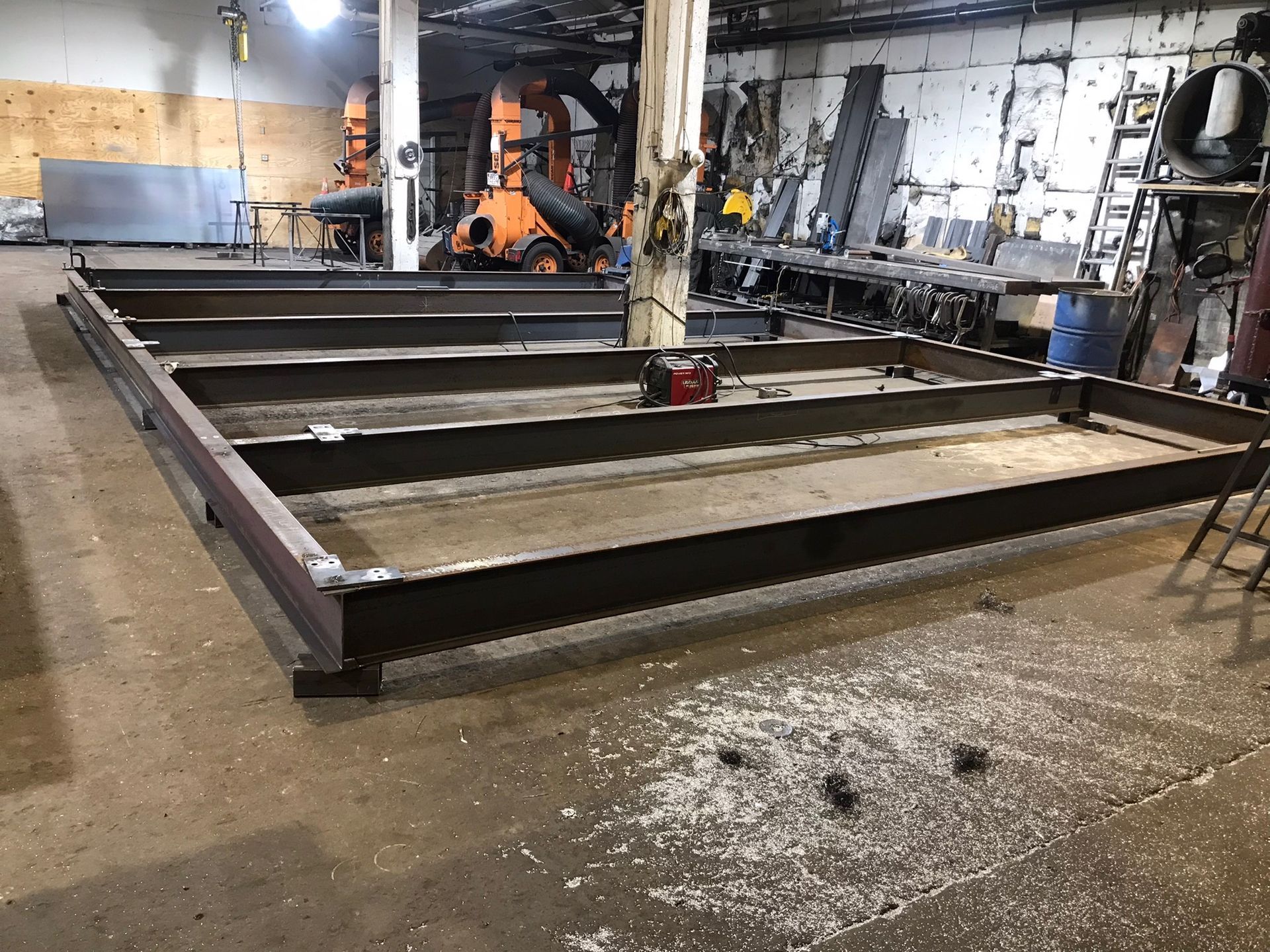 Large steel platform frame in an industrial workshop with concrete floor and machinery in the background