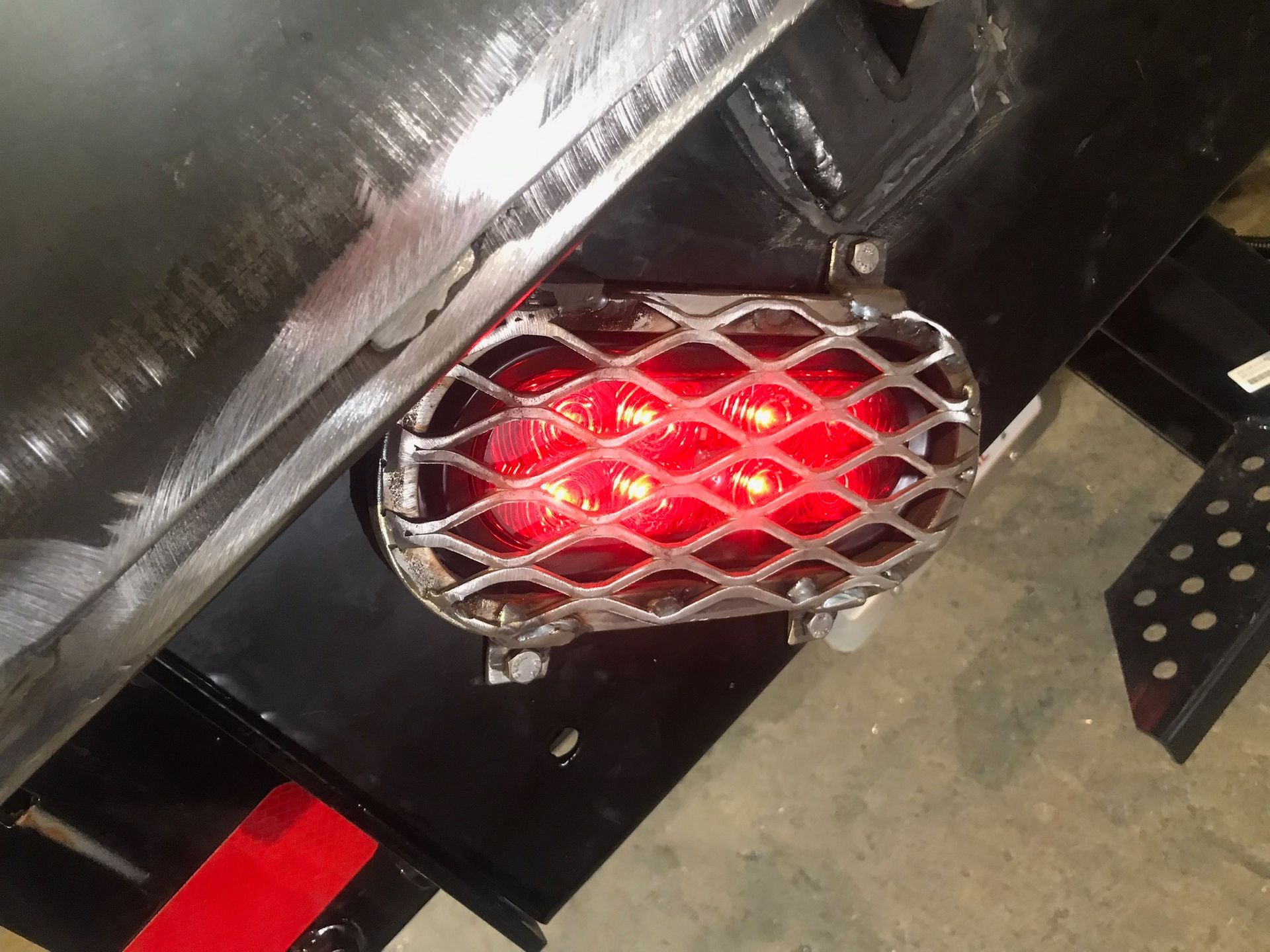 Close-up of a red taillight behind a chrome mesh guard on a black vehicle.