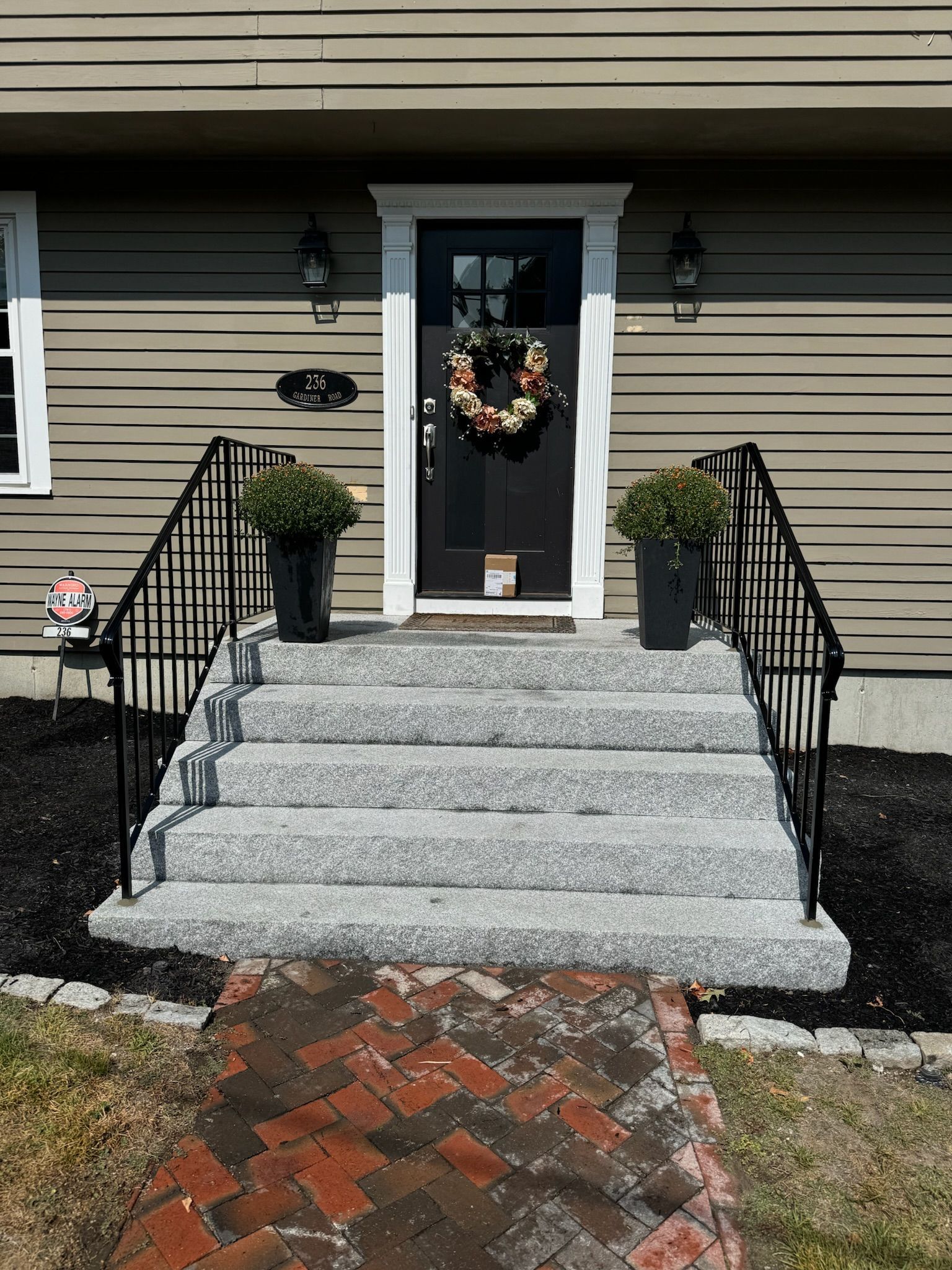 Front steps to a house with black door, fall wreath, and potted topiaries by black railings