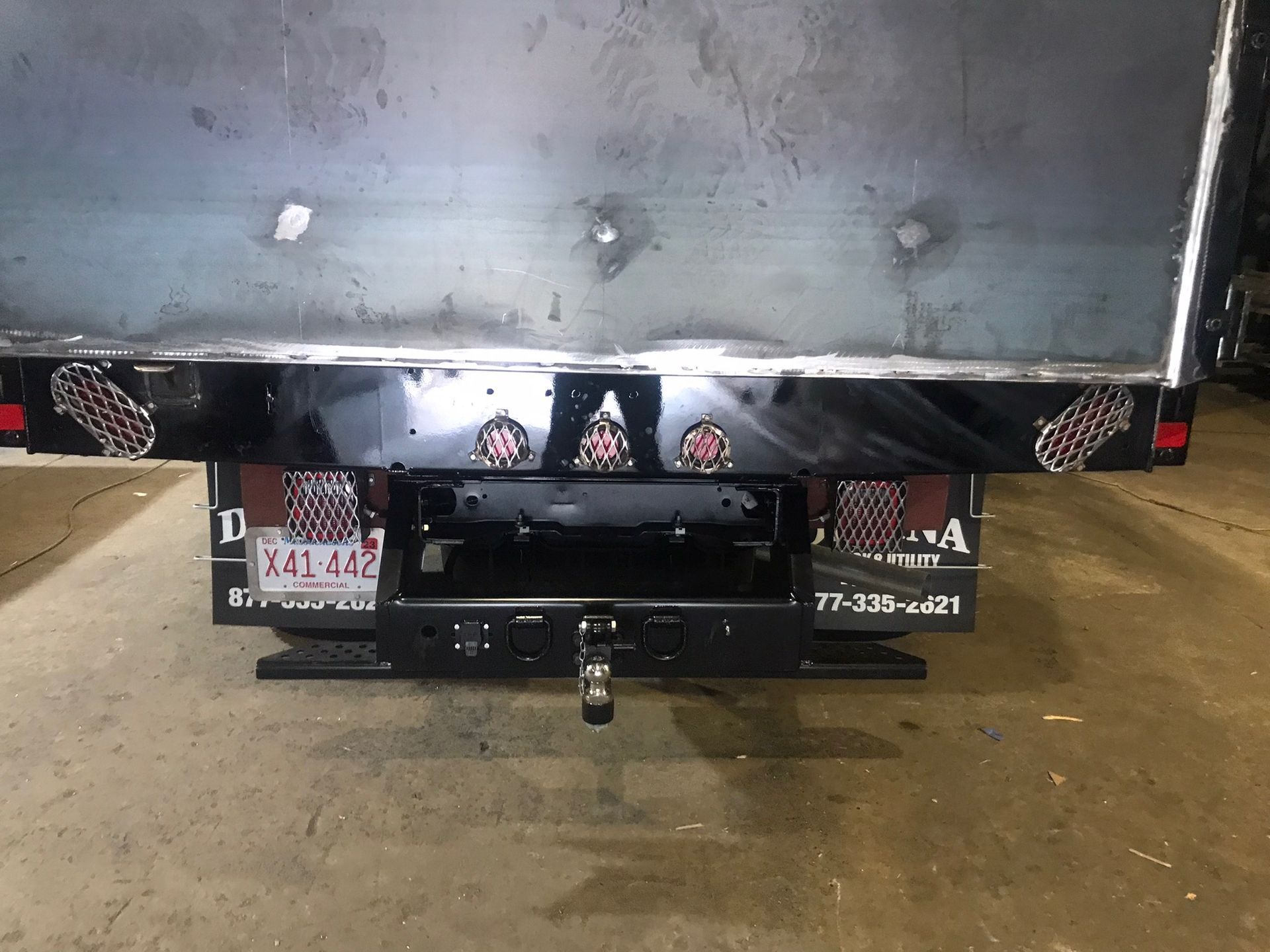 Rear view of a black truck with a trailer hitch and license plates, parked on a wet surface.