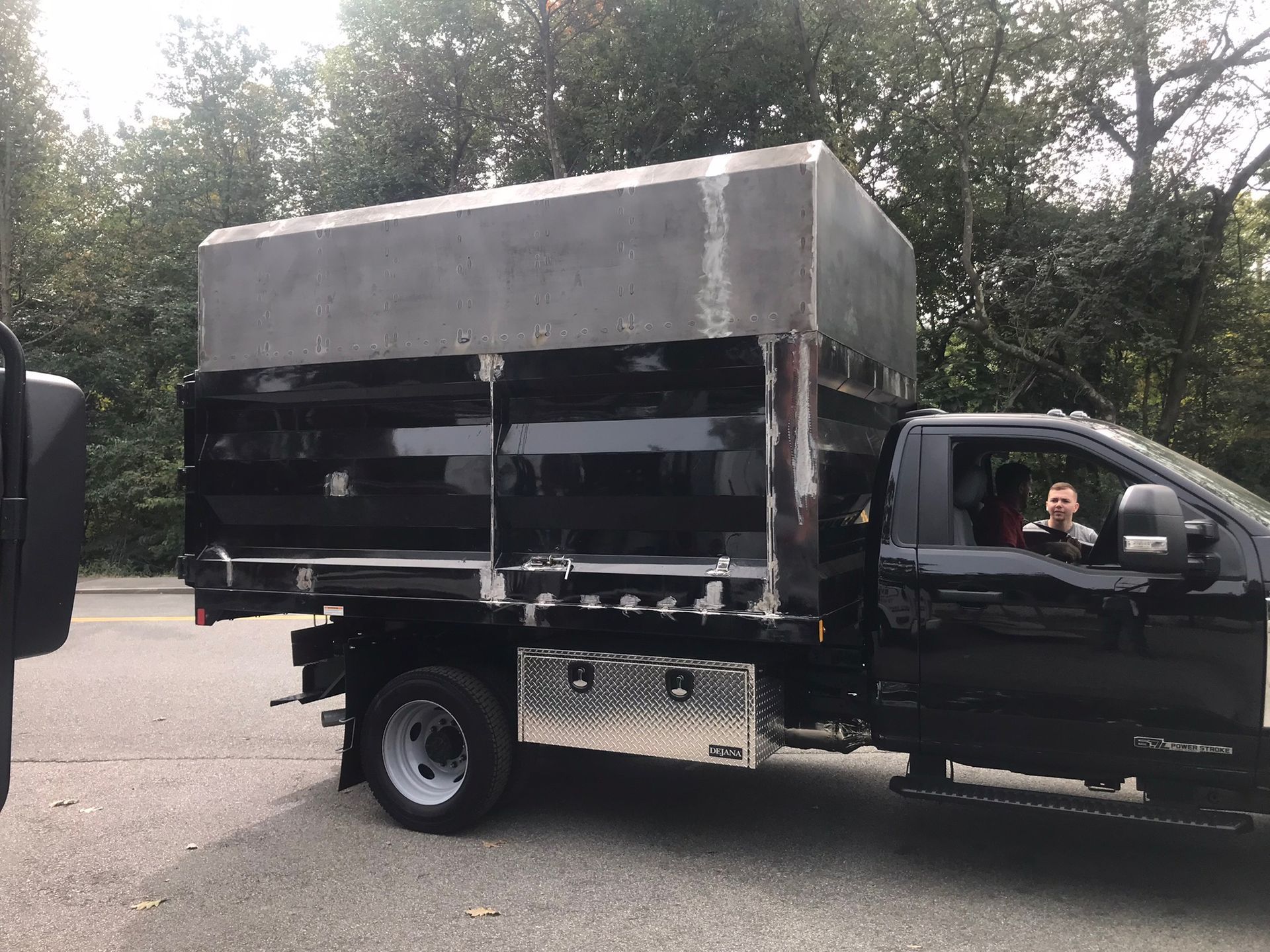 Black pickup truck with an open cargo bed and covered load parked on a road, driver visible inside