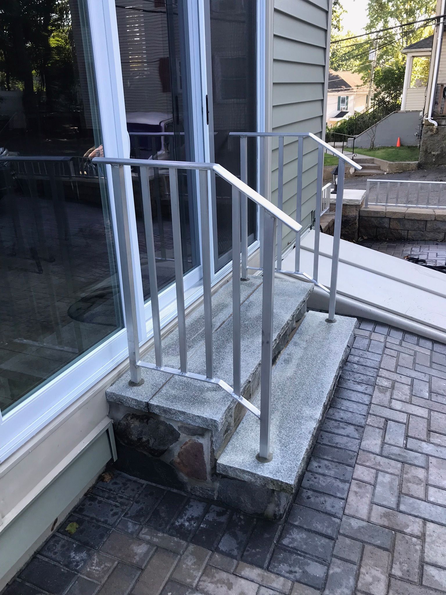 Front steps with metal railing beside a sliding glass door and paved patio.