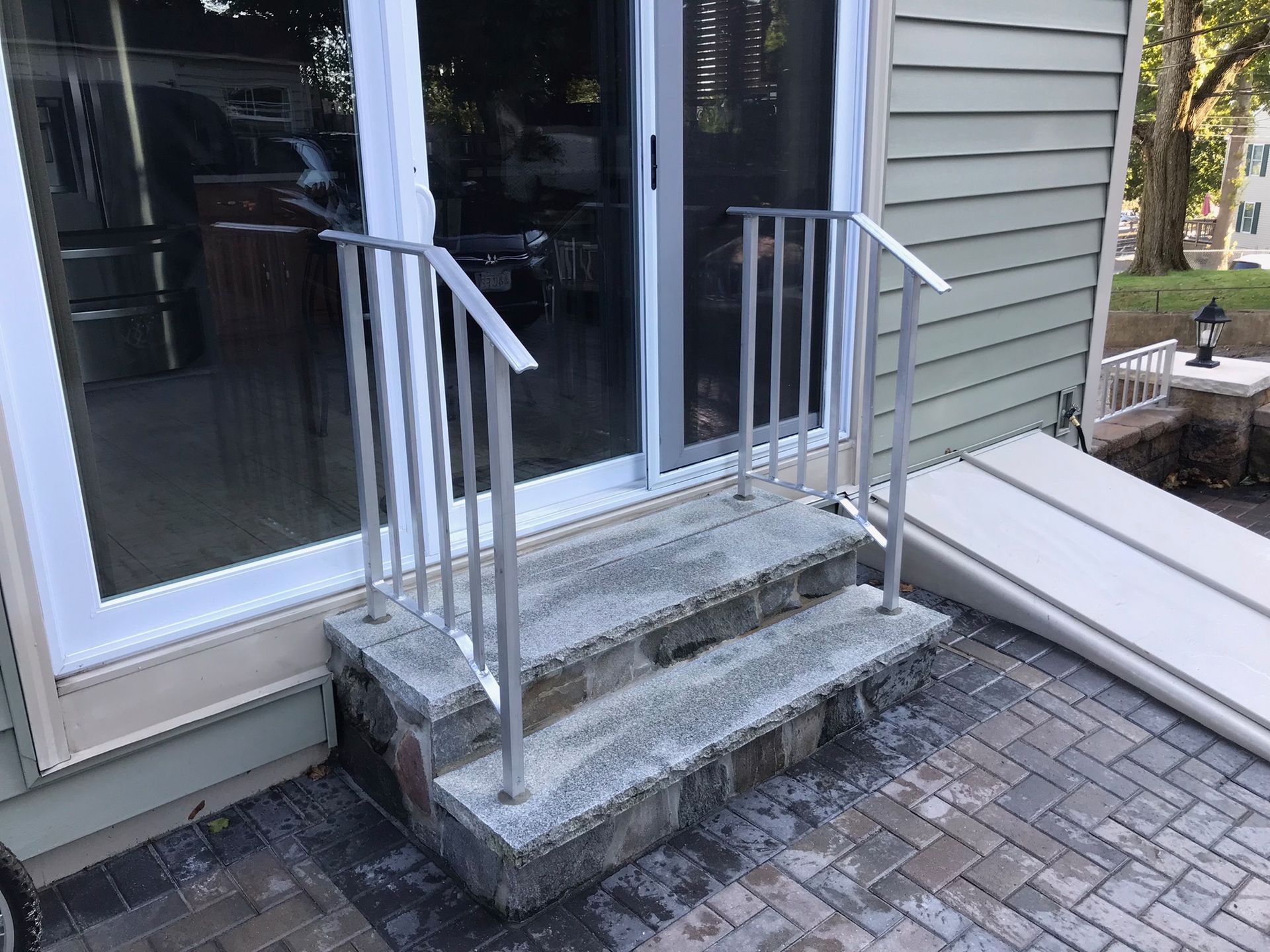 Concrete front steps with metal railings leading to a glass door beside a siding-covered porch.
