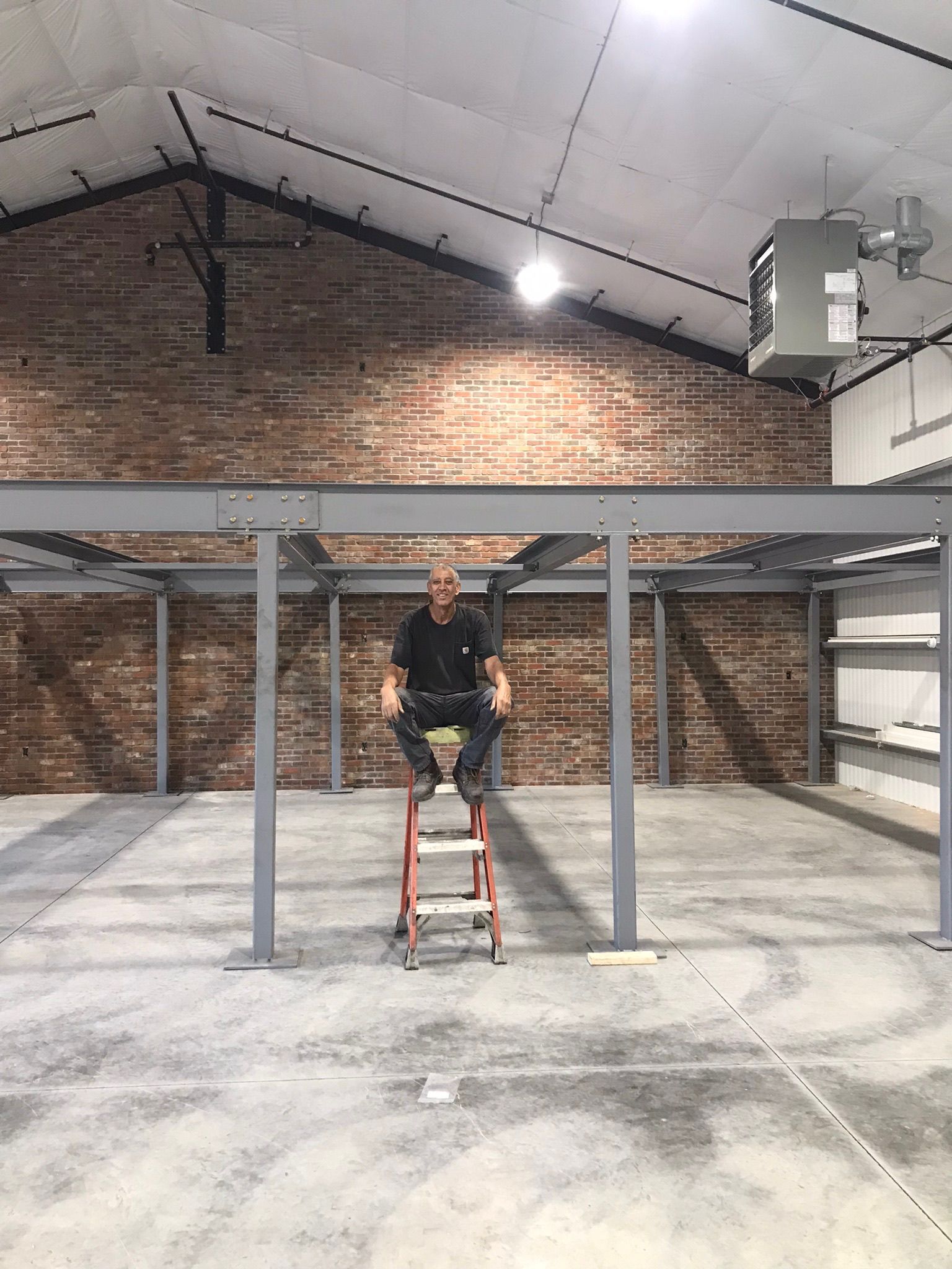Person seated on a red step ladder in an empty warehouse with brick walls and metal beams