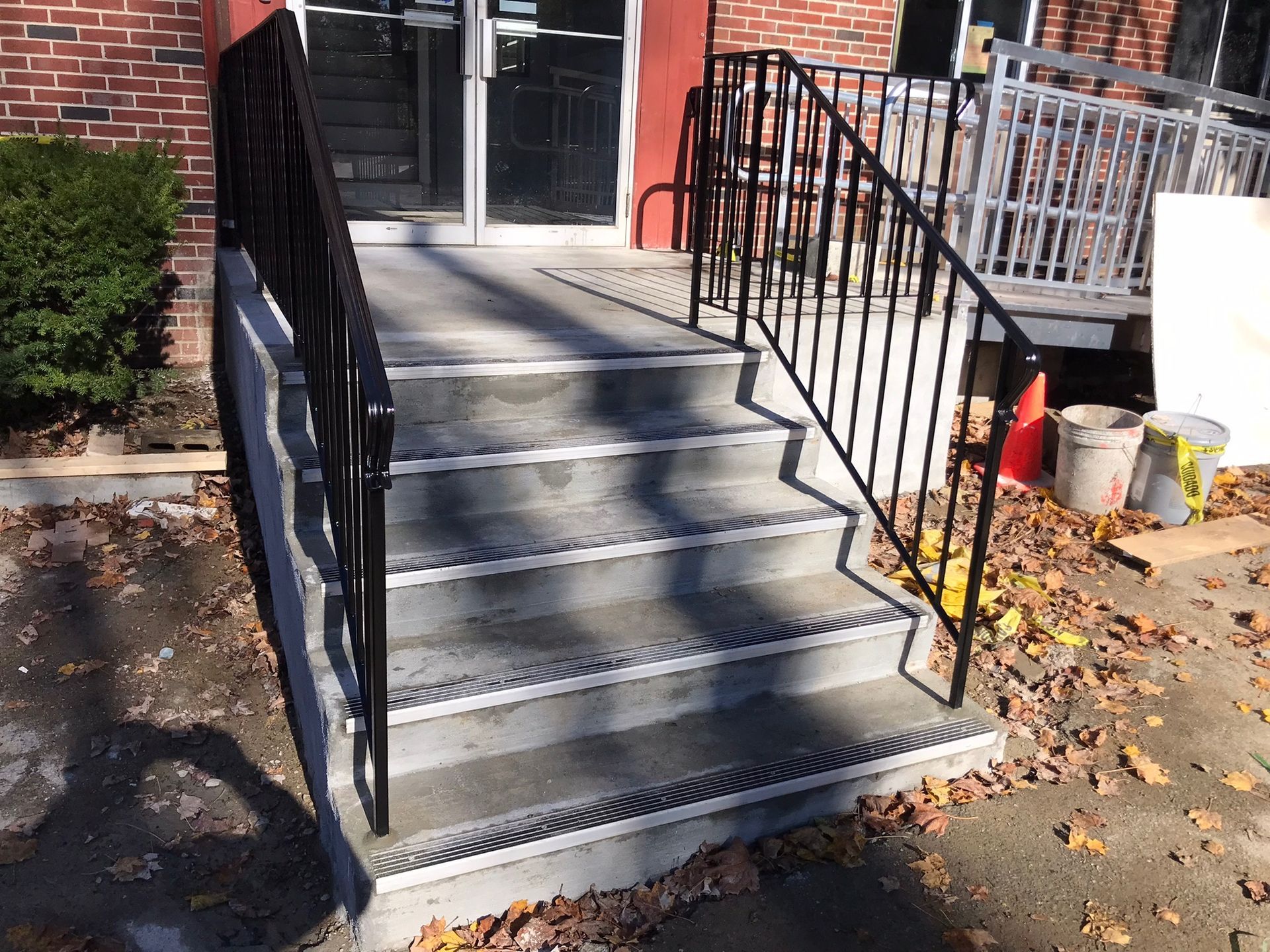 Concrete steps with black railings leading to a brick building entrance in sunlight