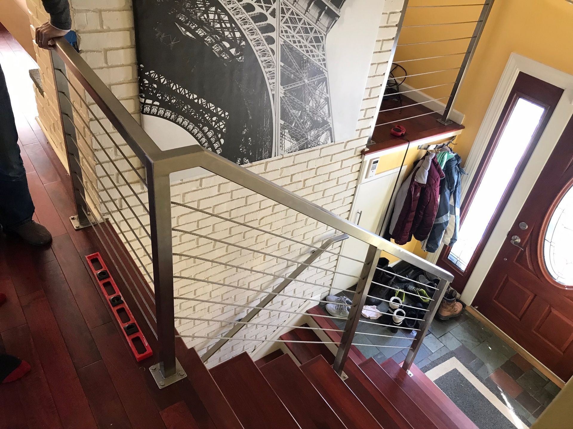 Indoor staircase with white brick wall, wooden handrail, and front door entryway below