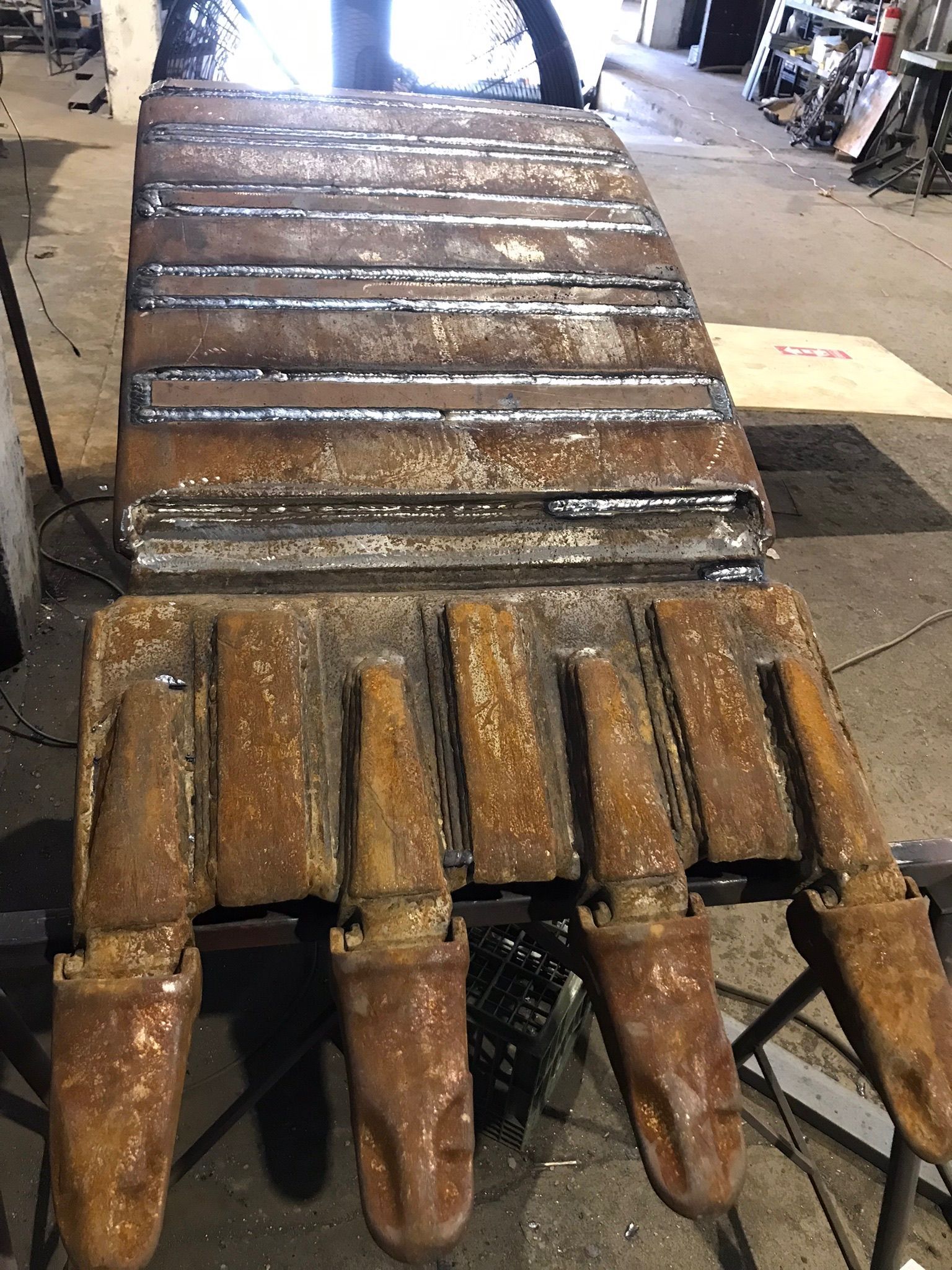 Rusty metal gate or machine part with pointed tines, viewed in a workshop-like setting