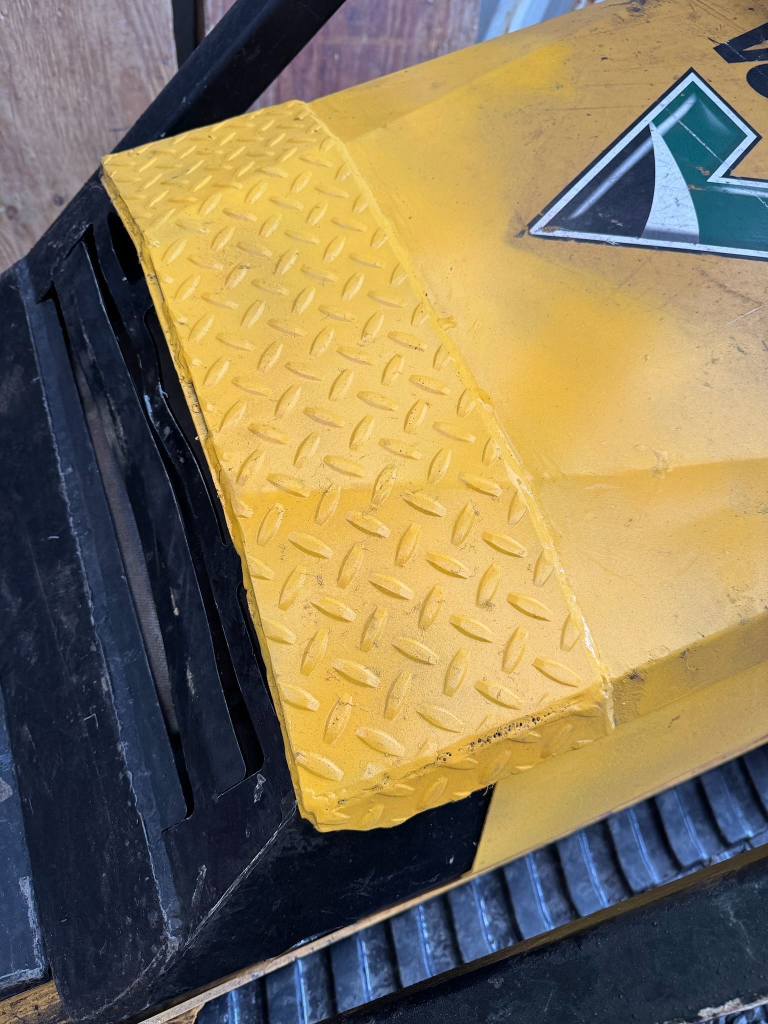 Yellow diamond-plate platform edge with black trim and a partial green-and-white logo.
