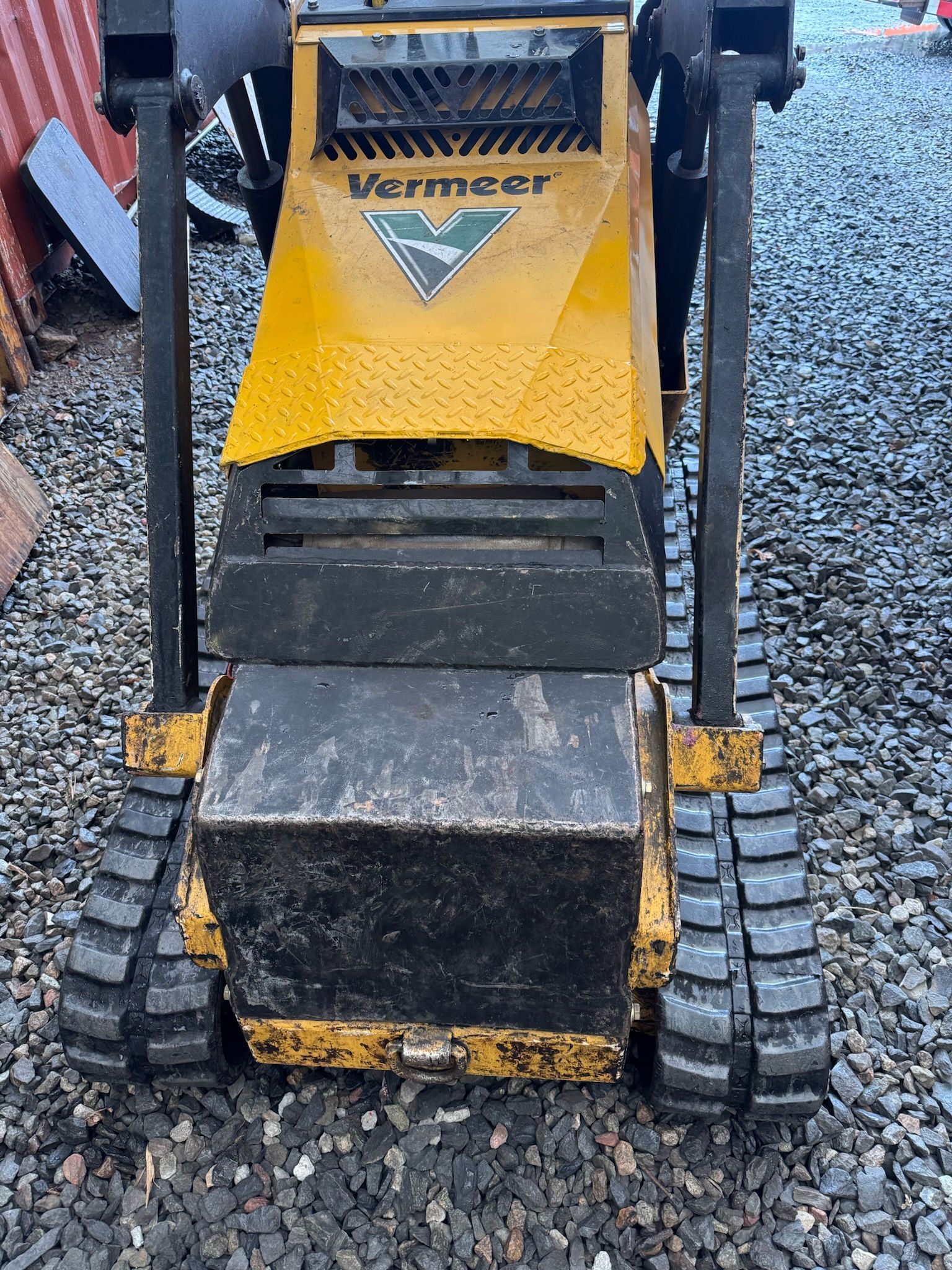 Yellow and black compact tracked construction machine parked on gravel