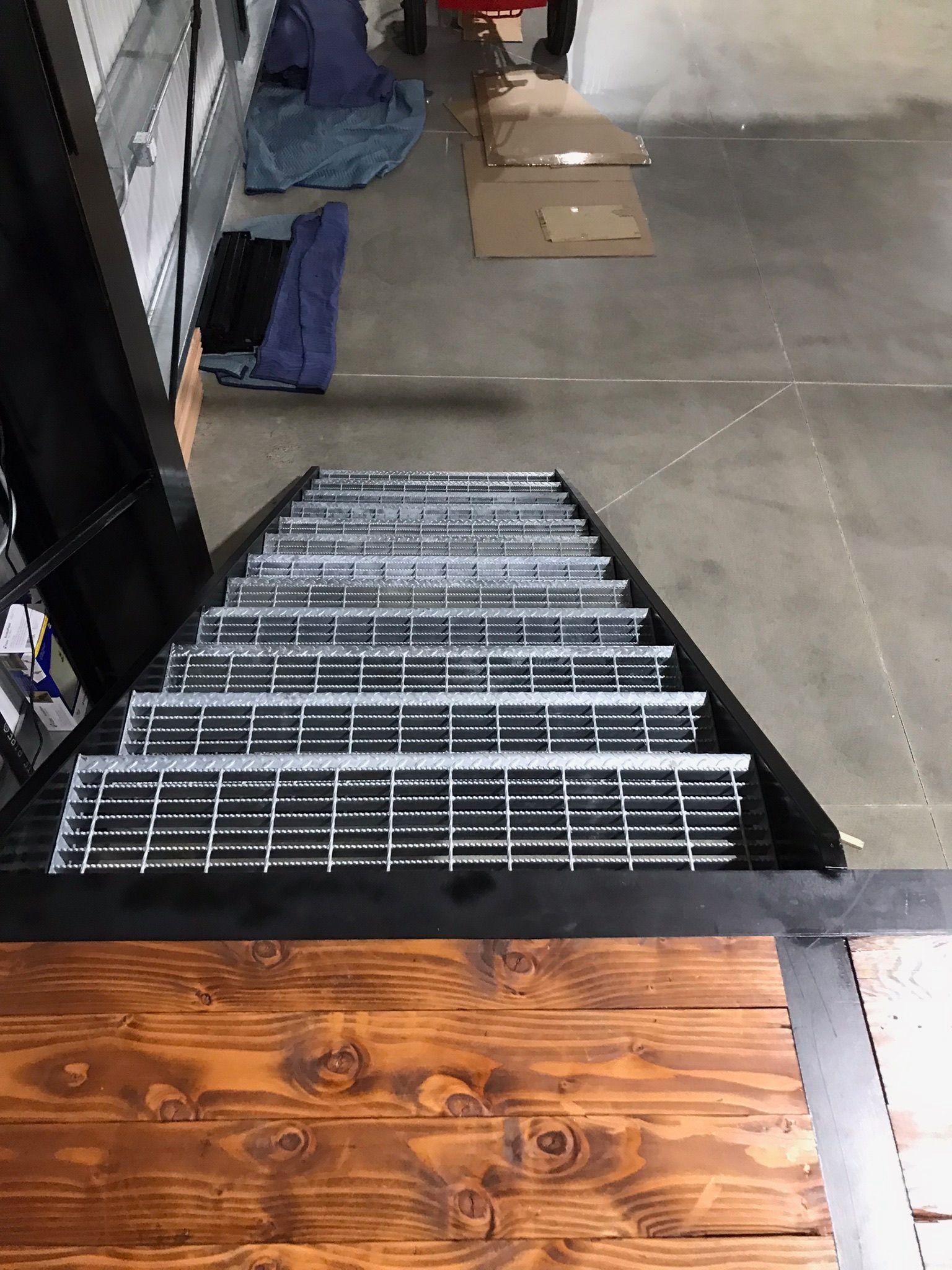 Looking down a metal staircase into a warehouse aisle with boxes and shelving, ending at a wooden platform.
