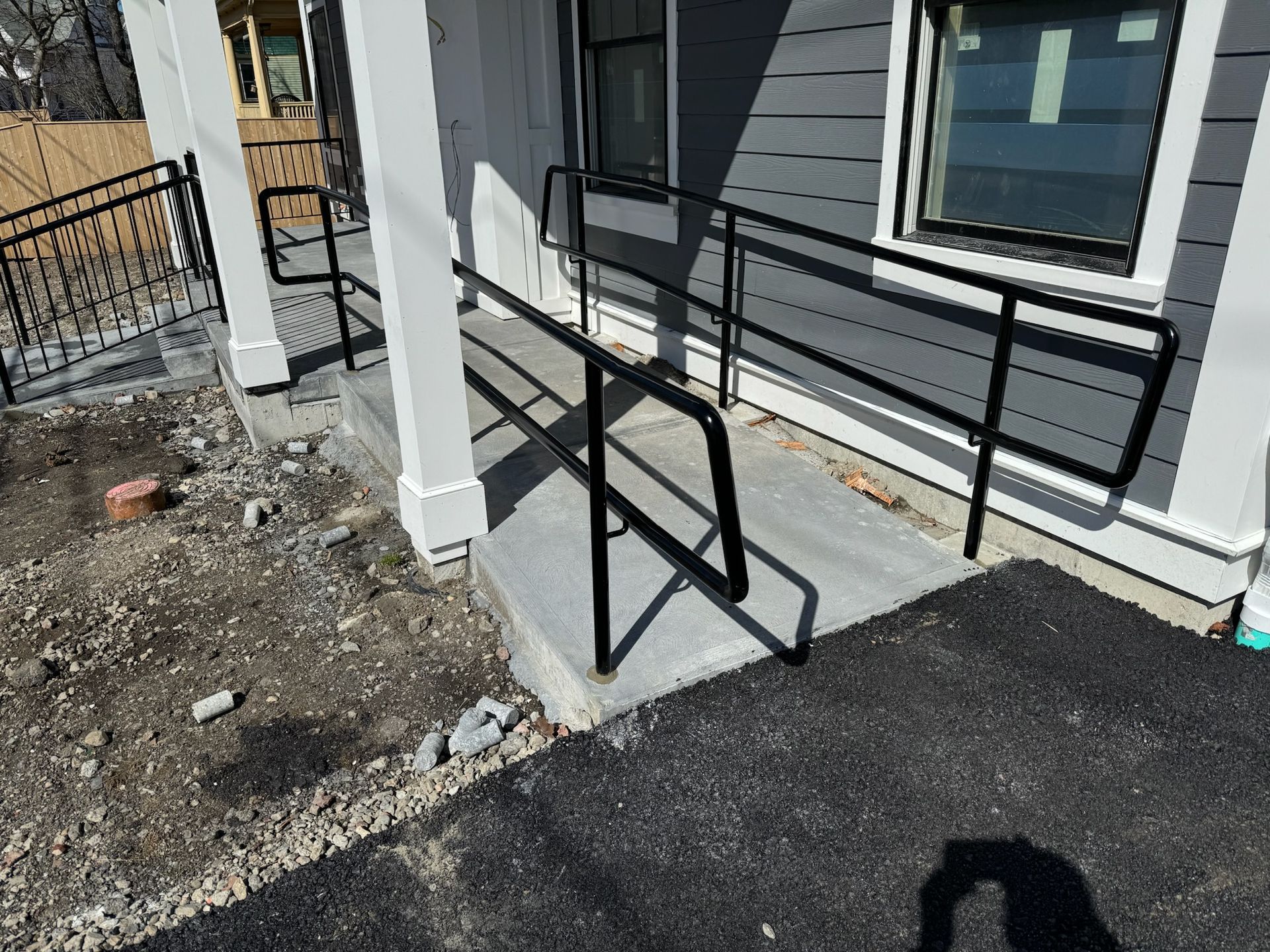 Exterior ramp with black handrails leading to a gray building entrance beside a gravel area