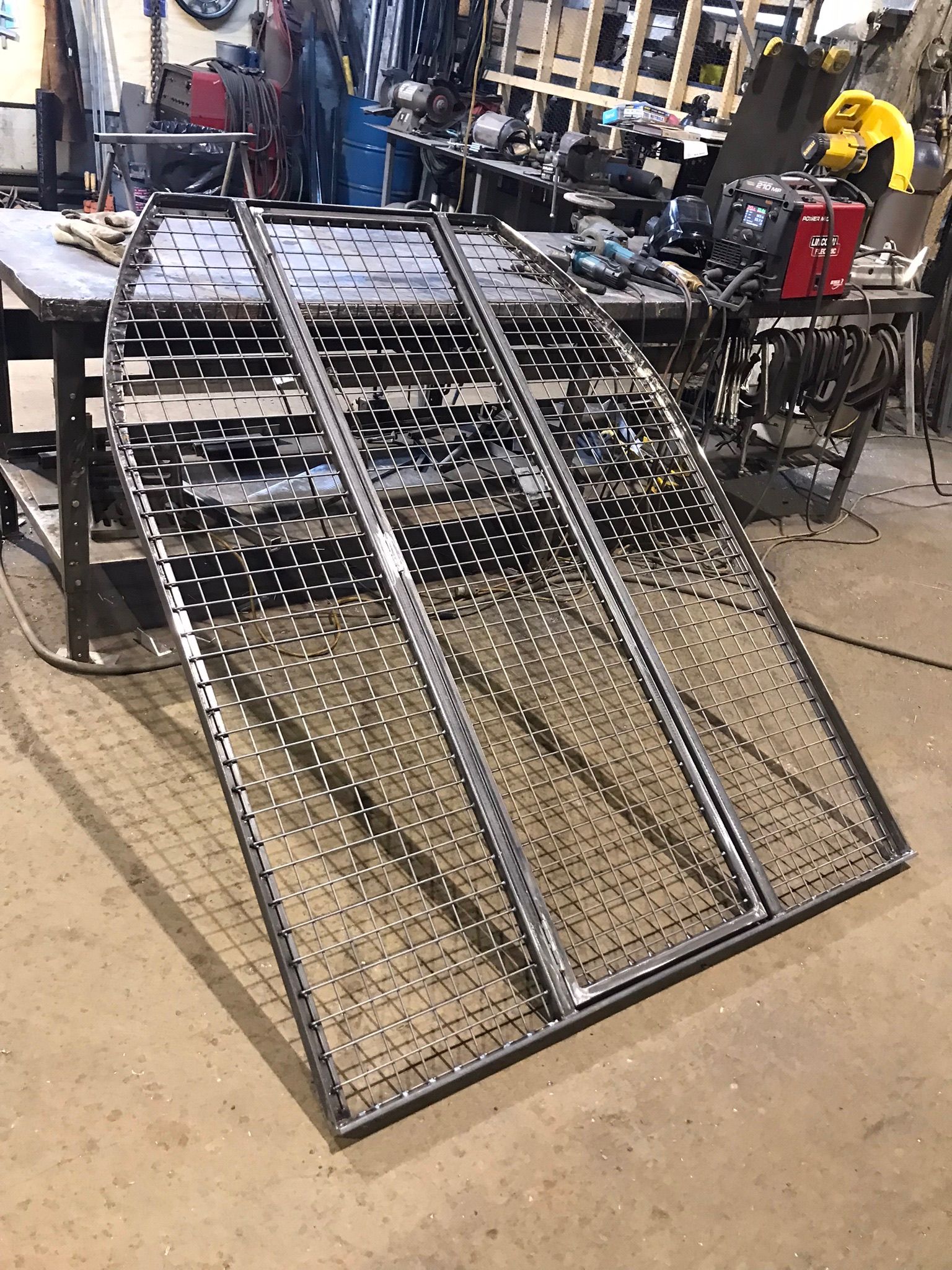 Metal wire ramp panels leaning in a workshop with tools and equipment in the background