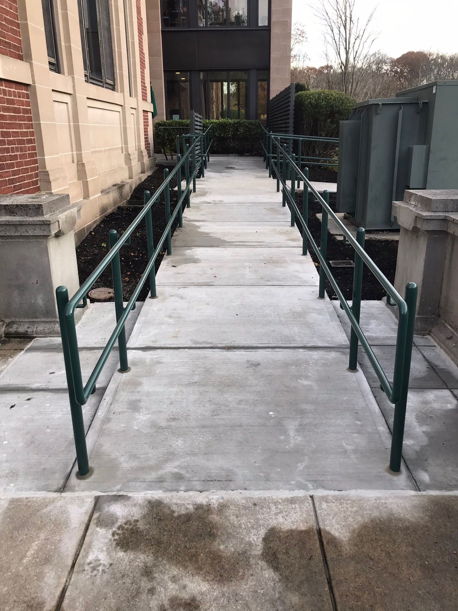 Concrete accessible walkway with green handrails leading to a building entrance