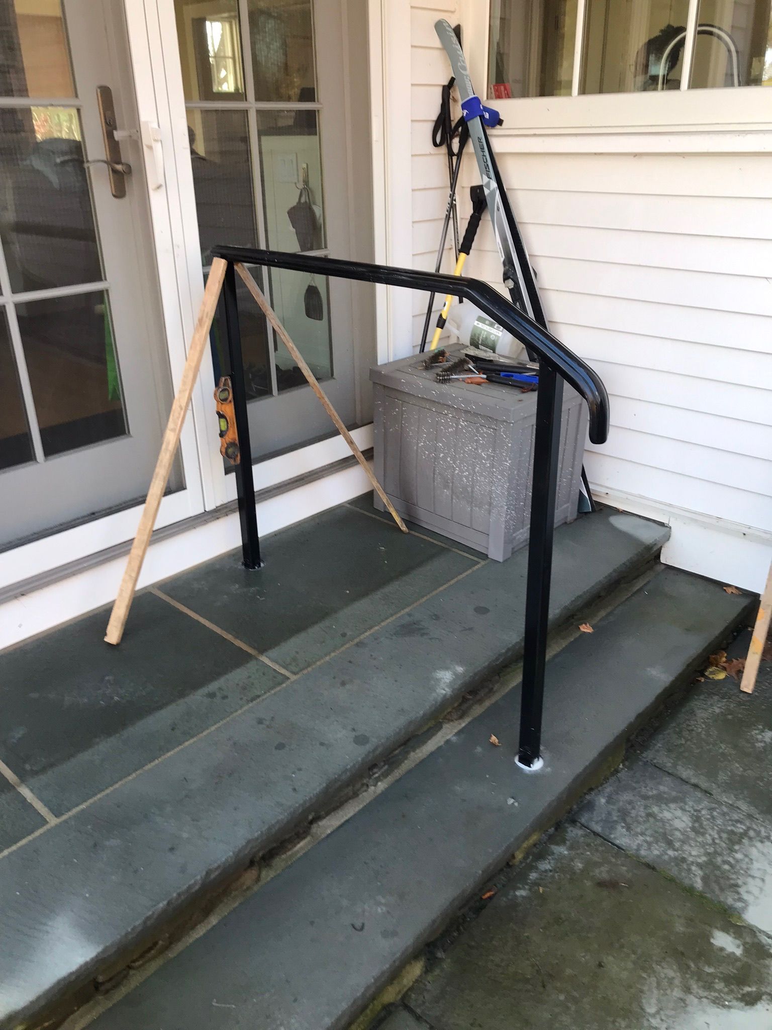 Front porch steps with a black handrail and cane leaning beside the door.