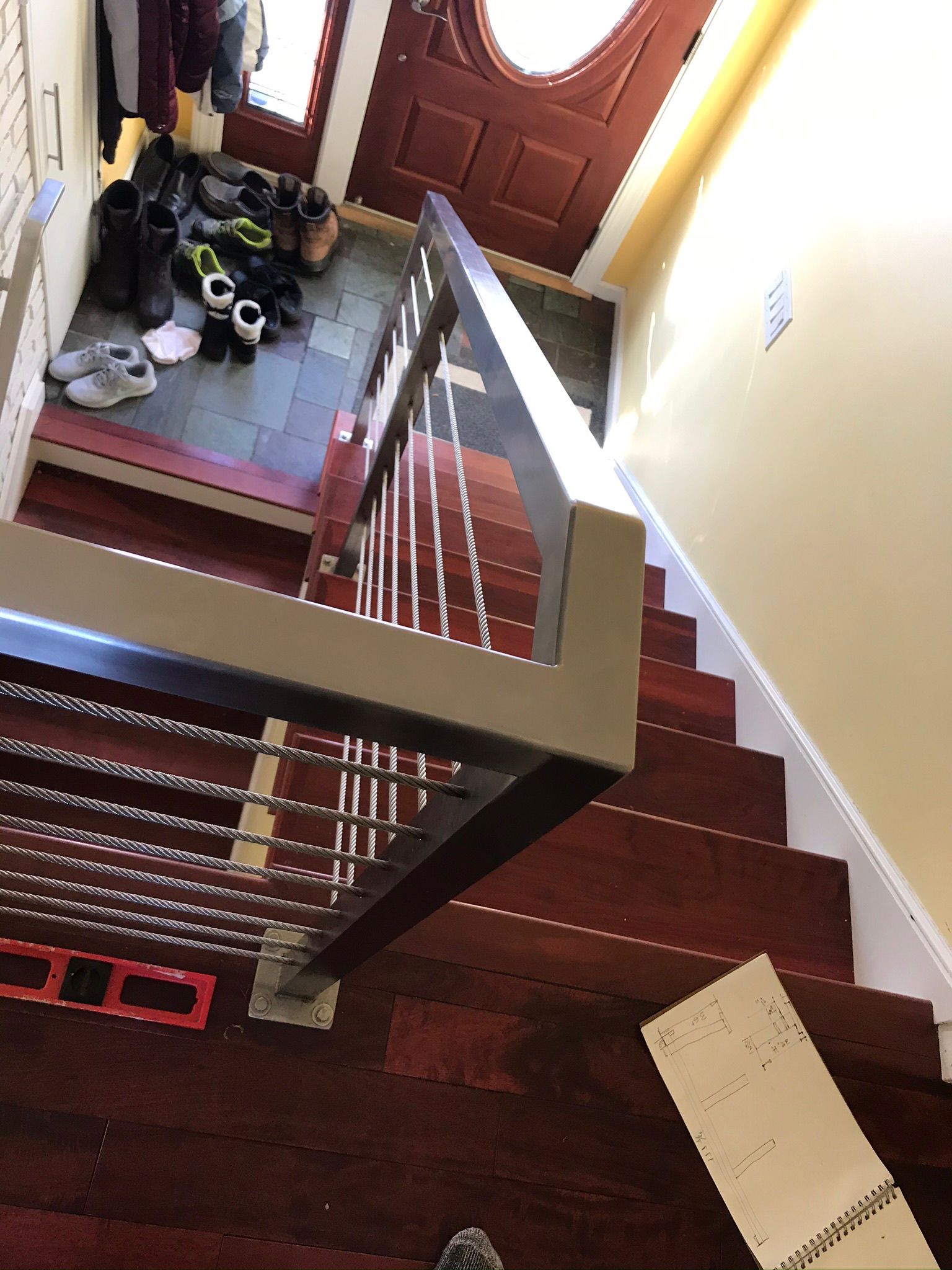 Stairwell with a red wooden banister, entryway door, and a bag of shoes by the landing.