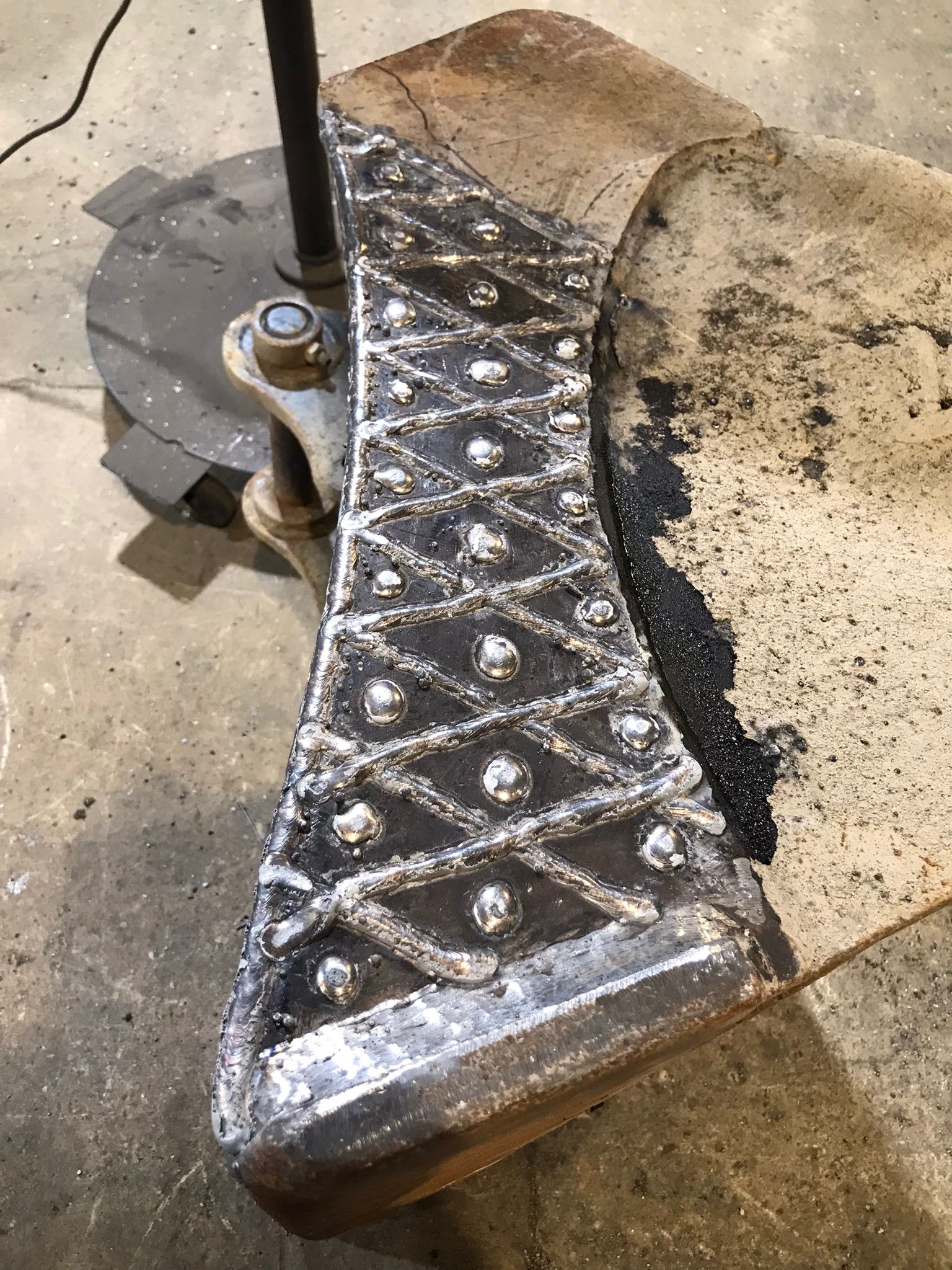 Cracked skateboard deck with black grip tape and silver diamond pattern on a concrete floor
