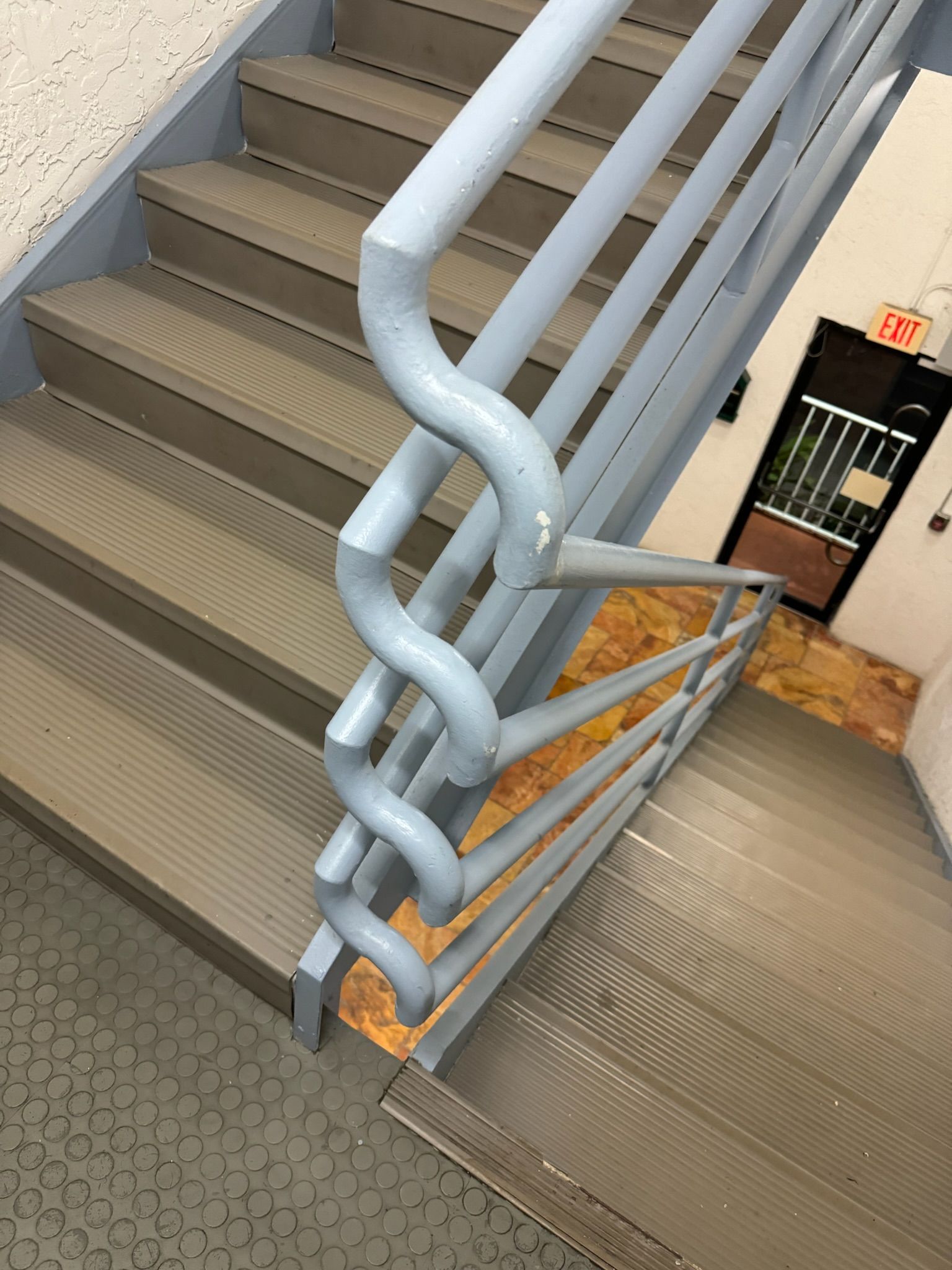 Stairwell with gray steps and a sculptural light-blue twisted metal handrail between floors