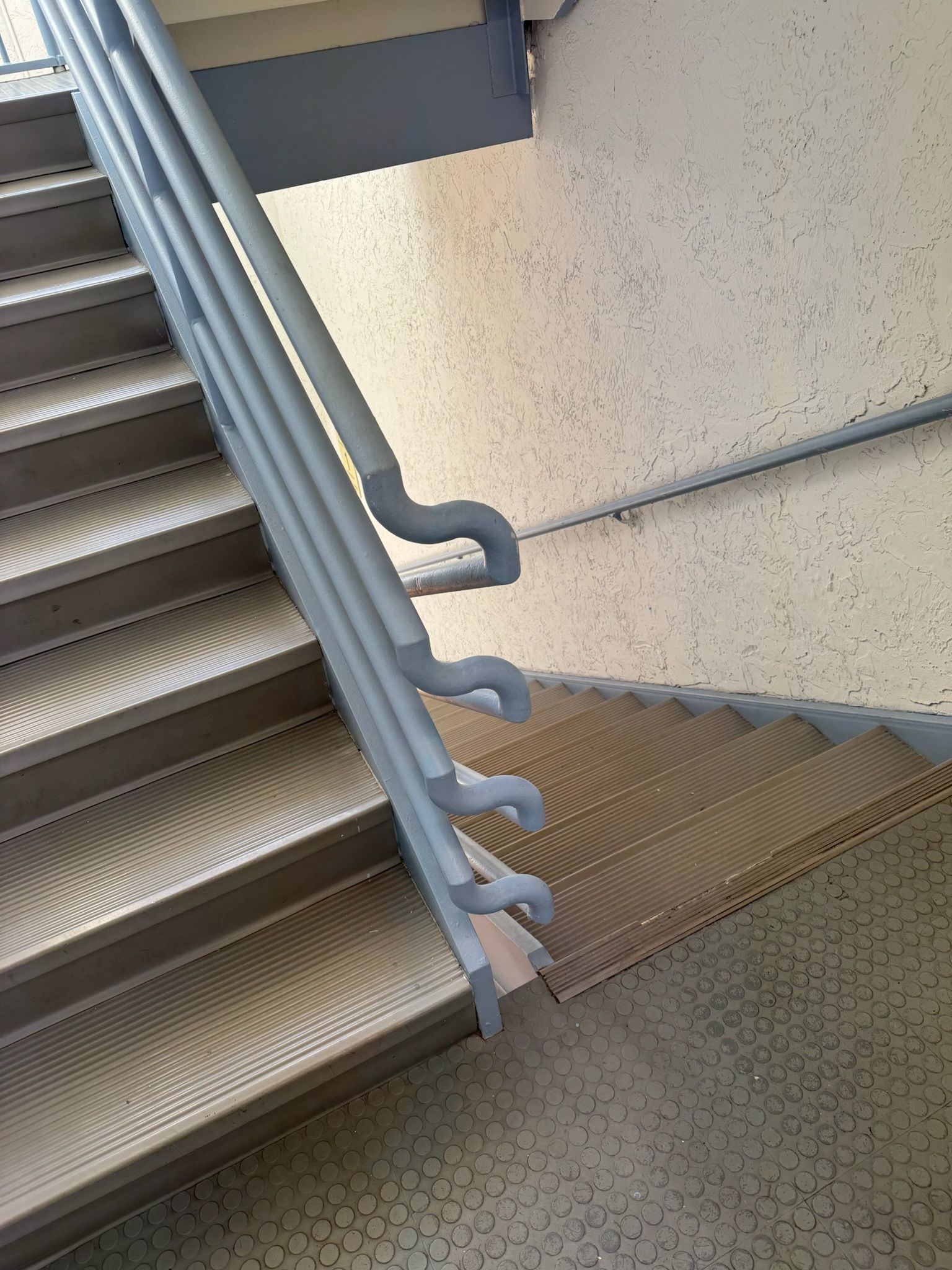 Staircase with gray metal handrail beside a speckled wall and grated landing.