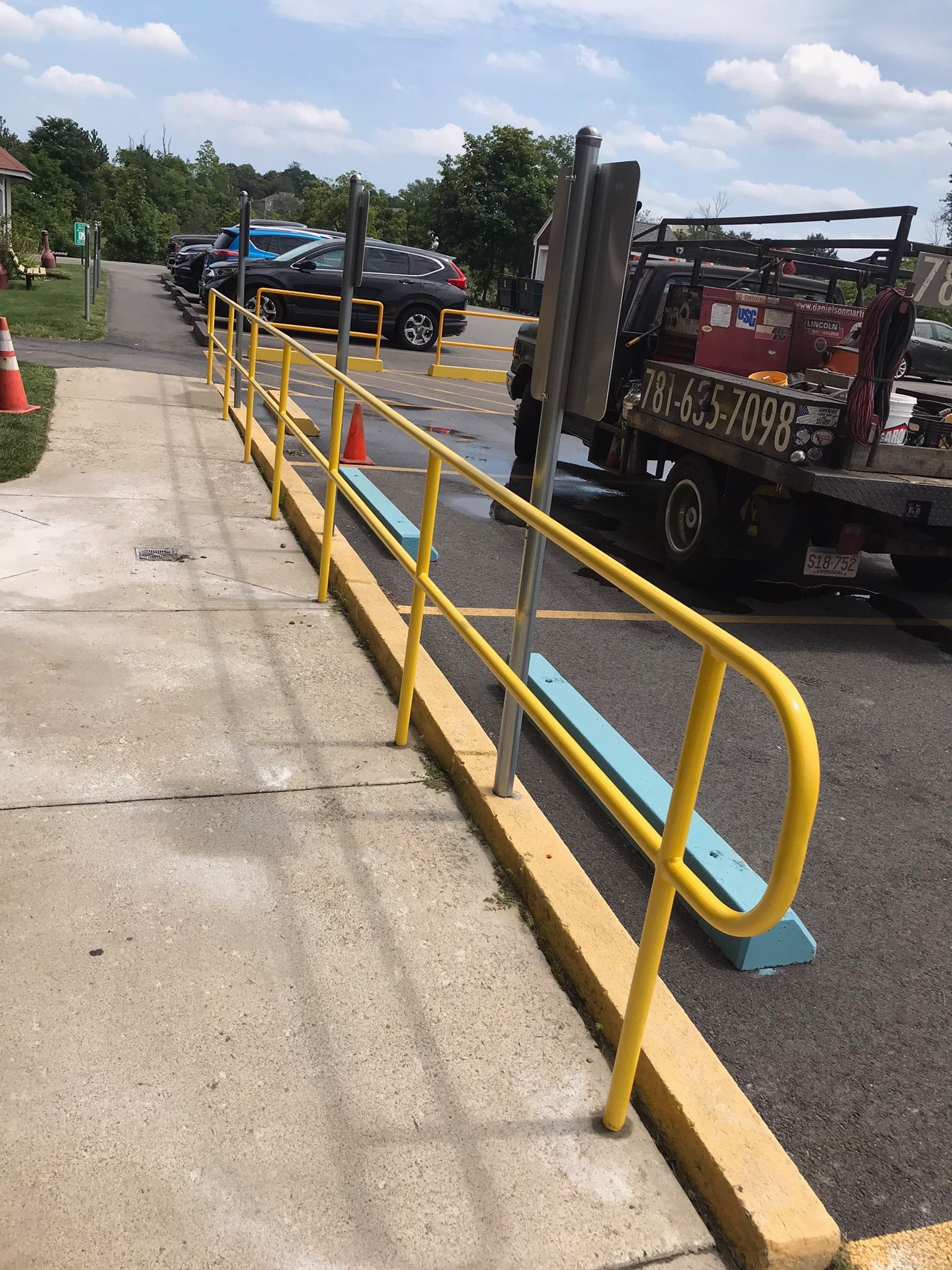 Yellow railings beside a loading ramp with parked vehicles on a sunny day