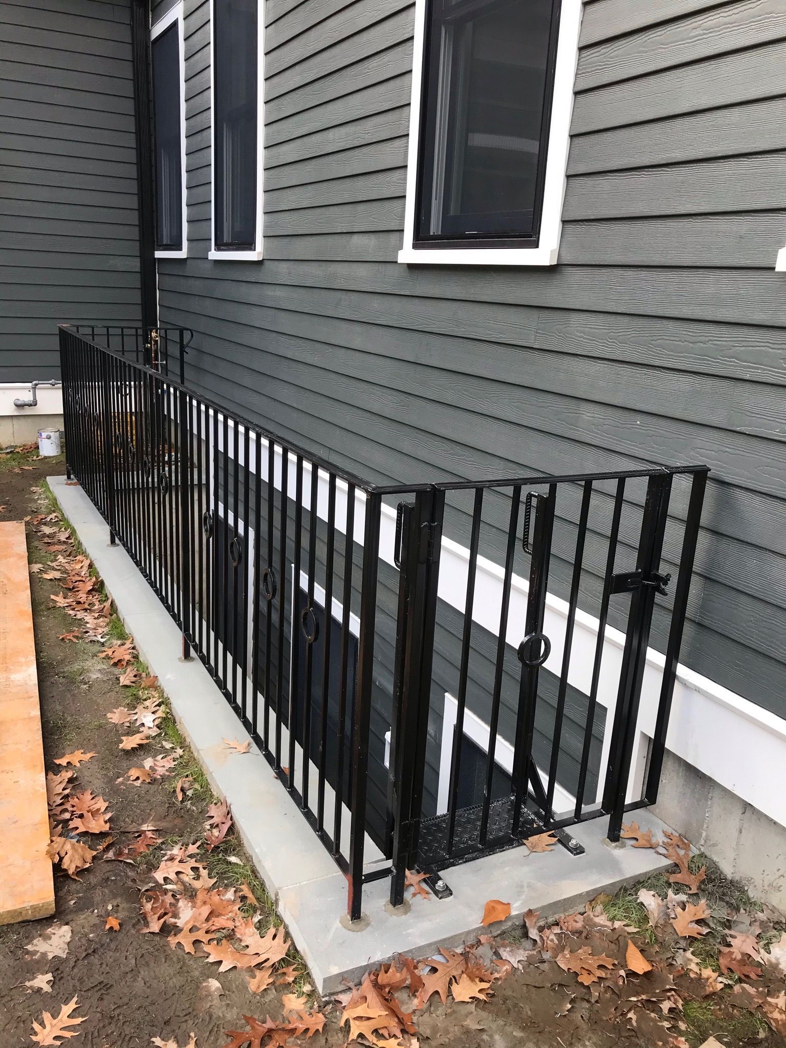 Black metal railing along a concrete basement stairwell beside a gray house with white-trimmed windows.