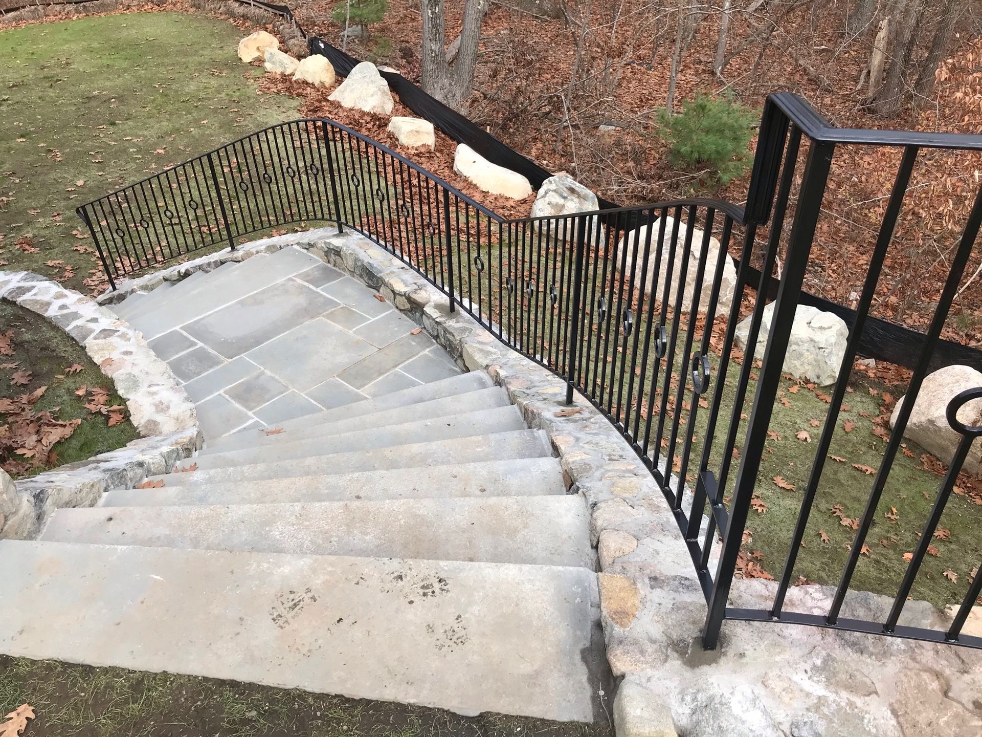 Curved outdoor stone staircase with black metal railing and rock landscaping below