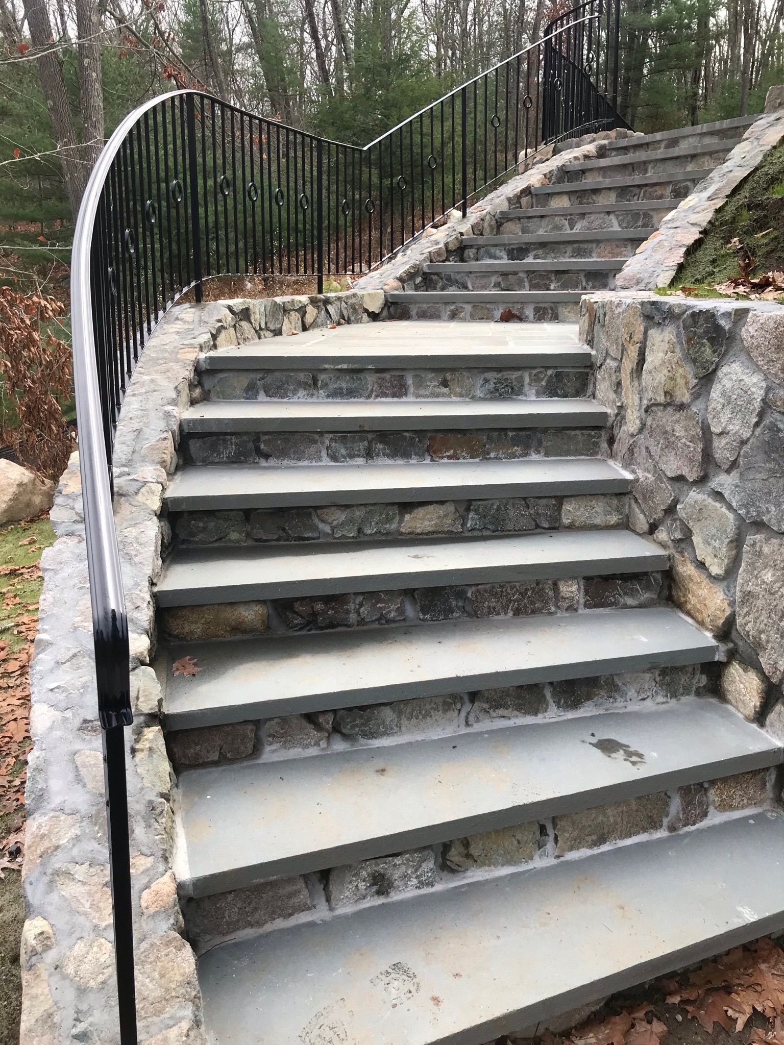 Outdoor stone staircase with black metal railings on a wooded hillside
