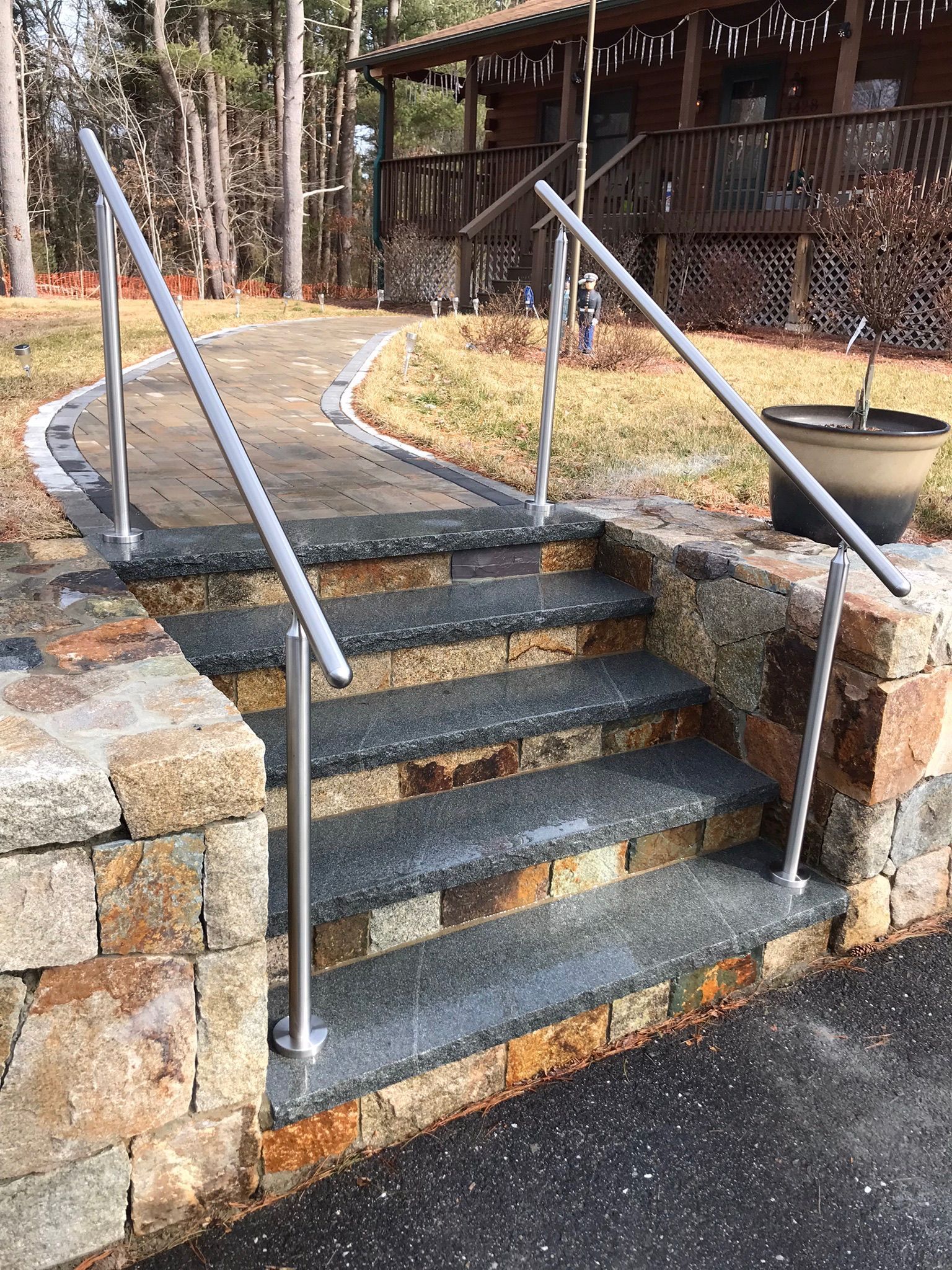 Stone outdoor steps with metal railings leading up to a wooden deck in a wooded yard