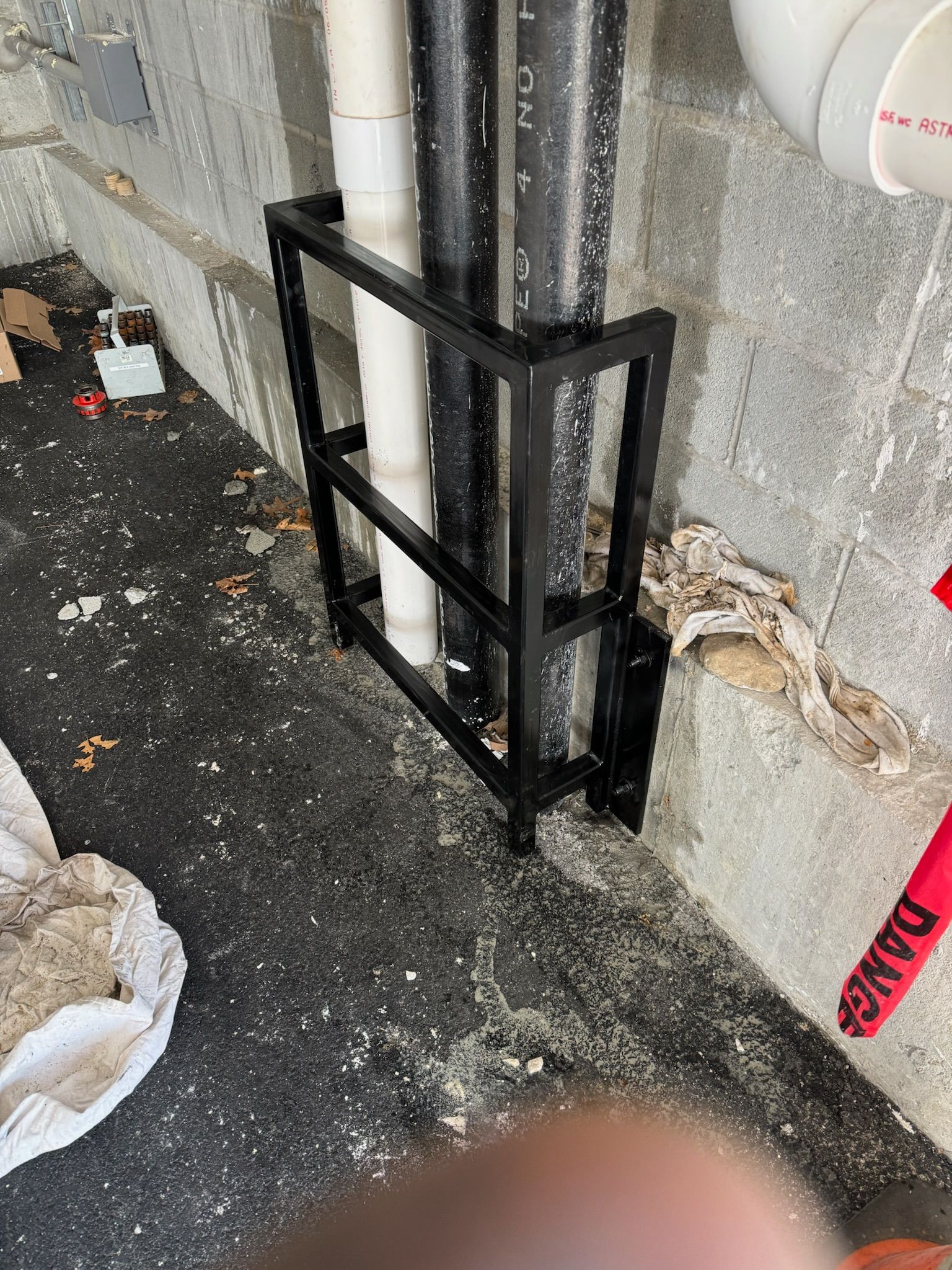 Black metal pipe support mounted on a concrete wall beside scattered debris on the floor