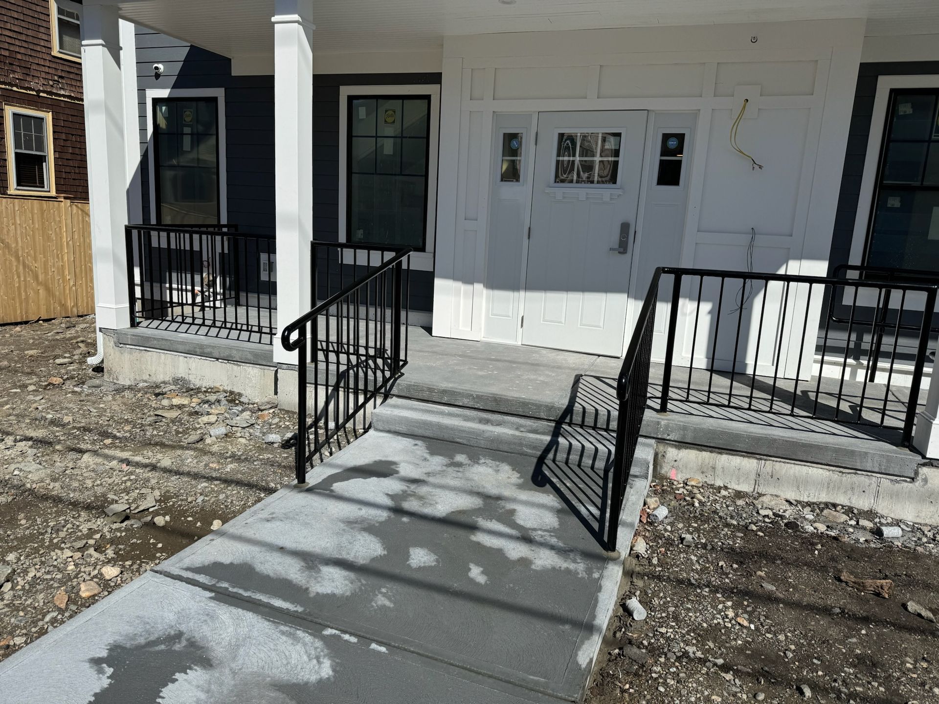 Front entrance with concrete ramp, steps, and black railings leading to white double doors.