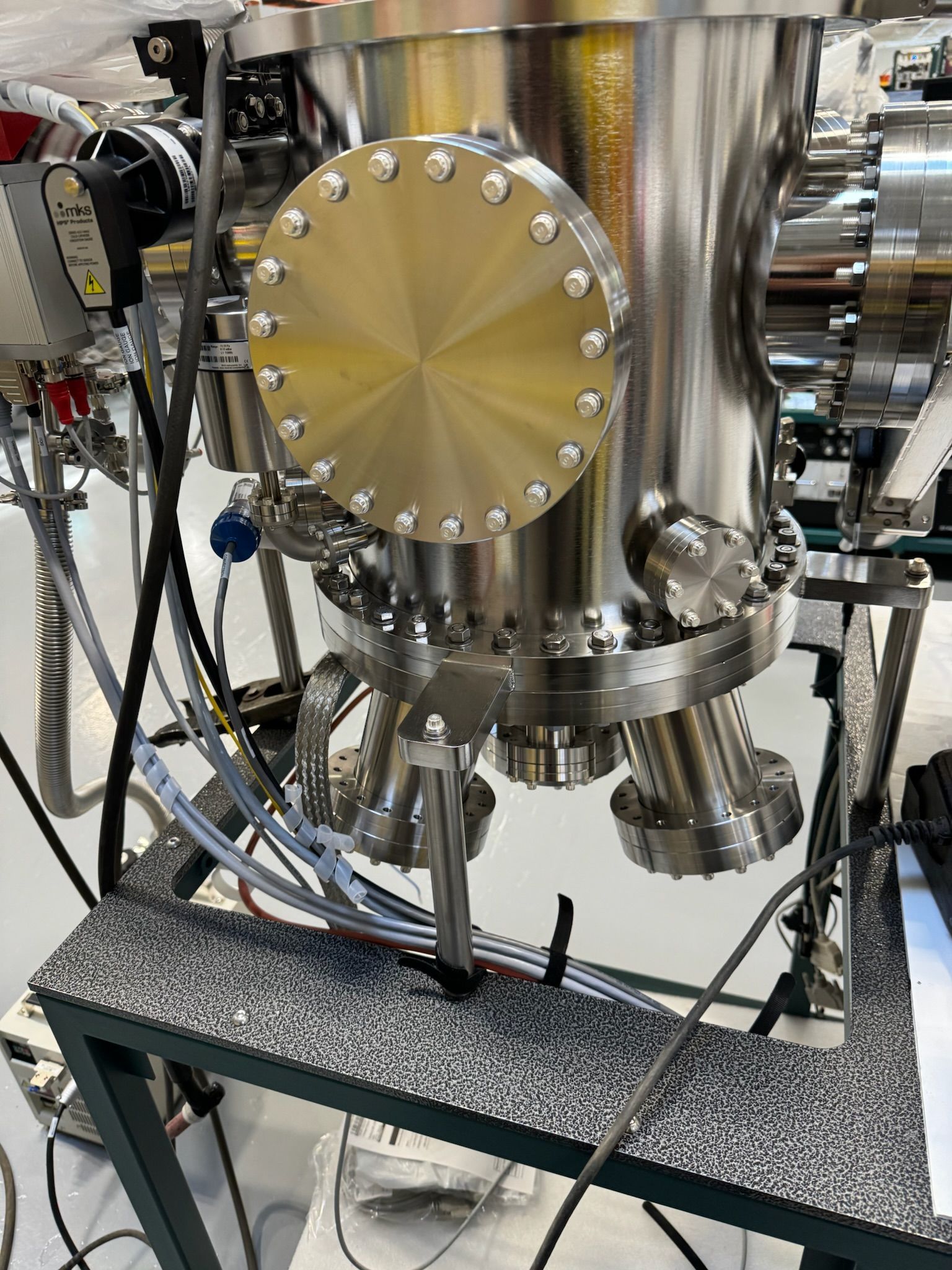 Polished stainless-steel vacuum chamber with bolted circular panel and attached tubing on a metal frame