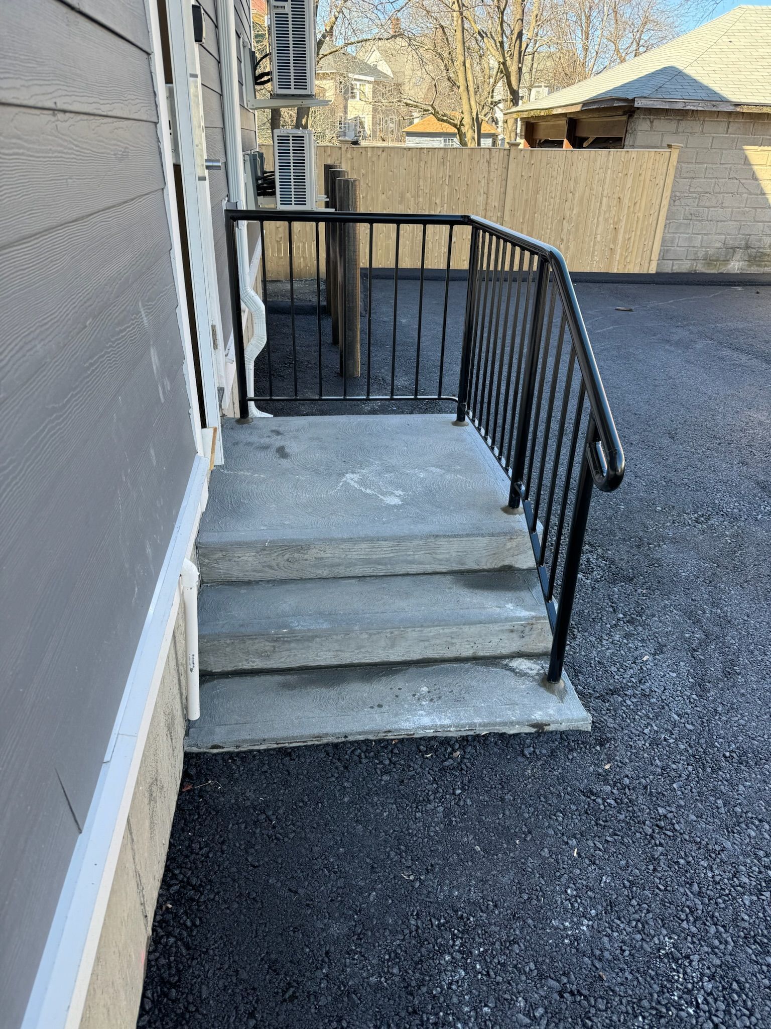 Concrete steps and black metal railing leading to a back door on a residential exterior landing.