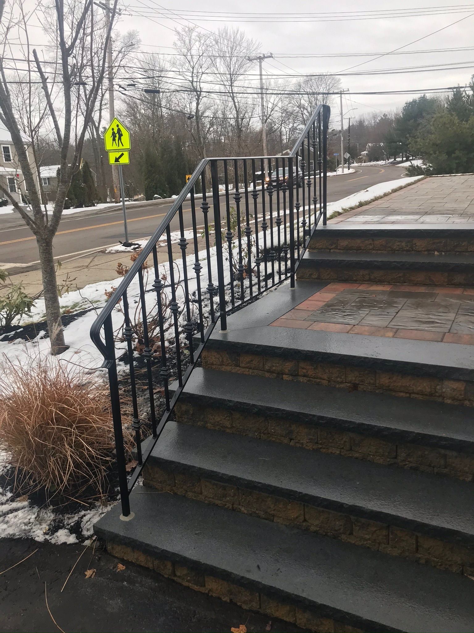 Outdoor steps with black railings beside a wet, snowy walkway and road