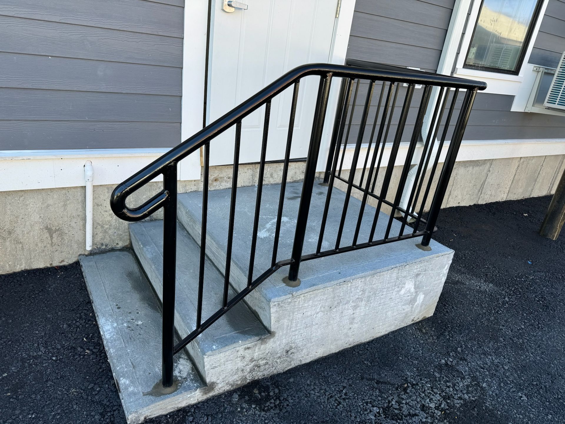 Black metal handrail on concrete steps leading to a raised porch entrance.