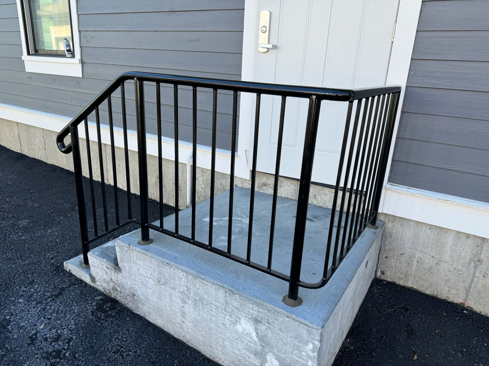 Black metal ramp railing on a concrete step outside a gray building entrance