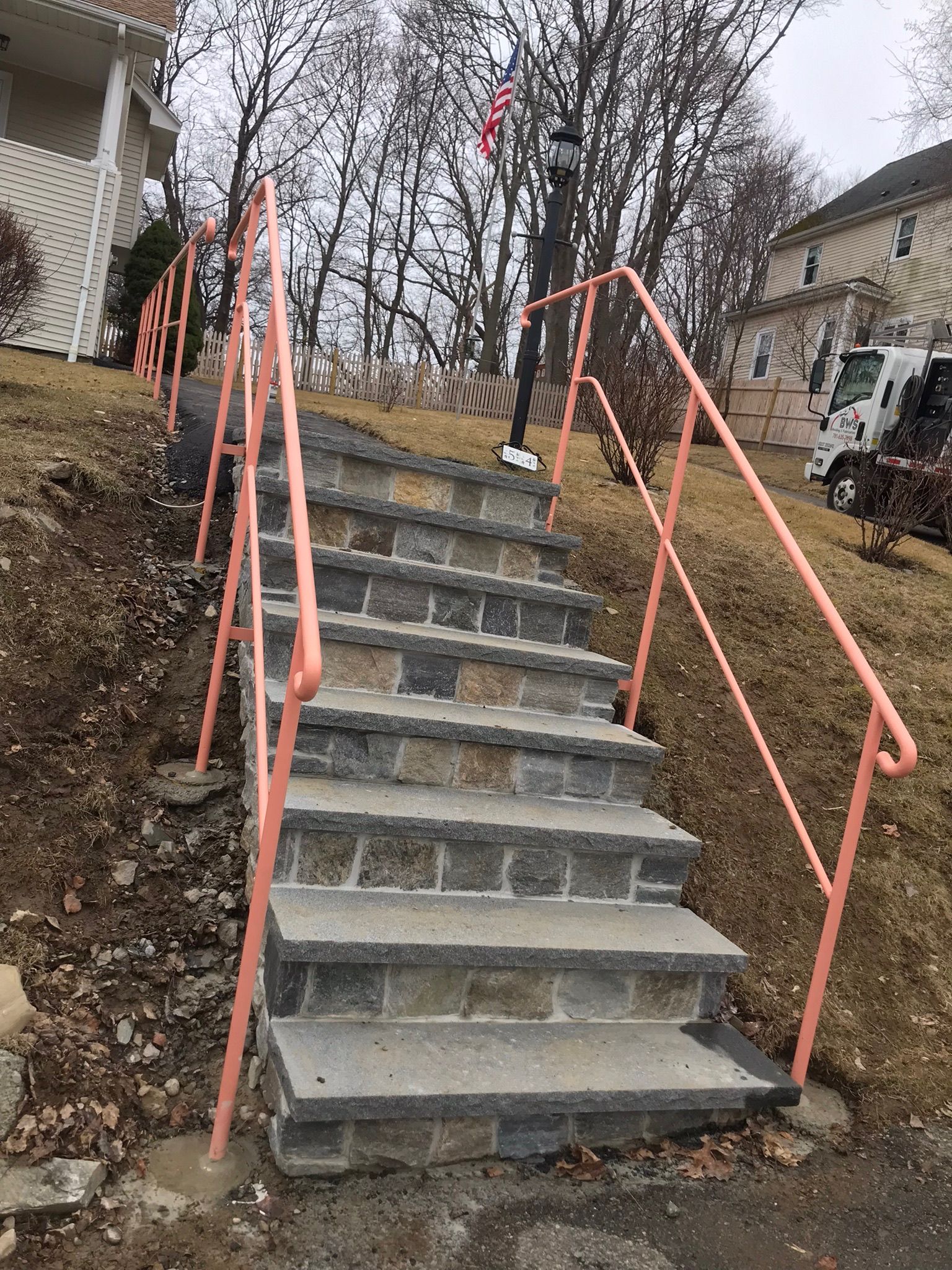 Outdoor concrete stairs between houses with orange handrails on both sides.