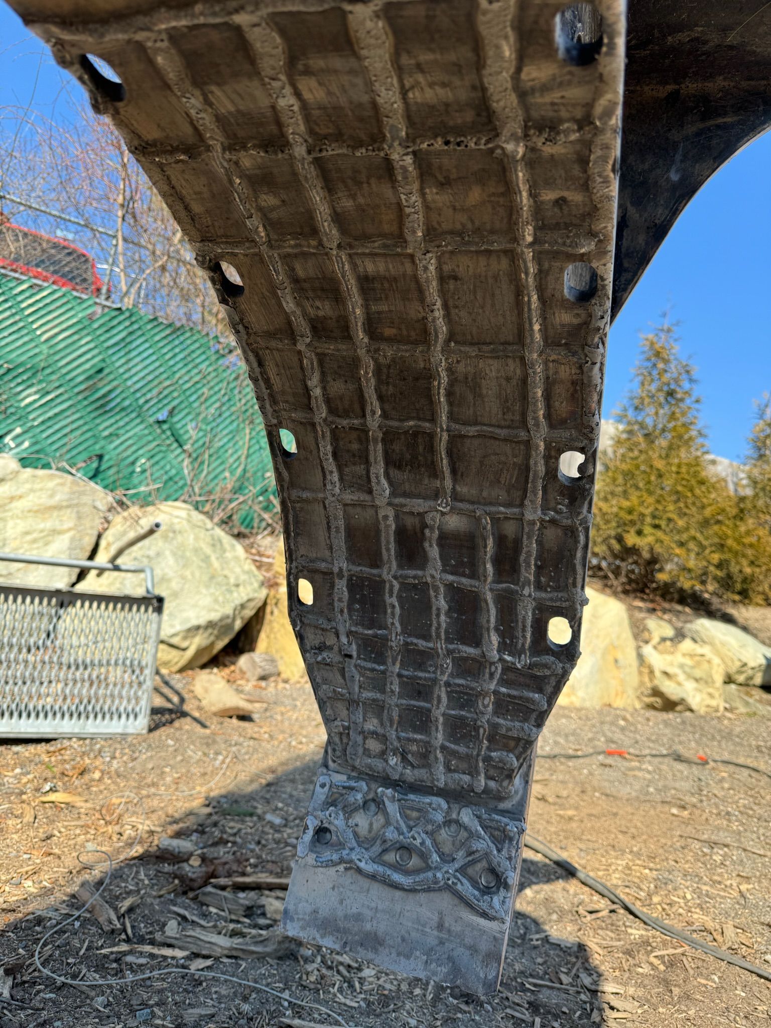 Close-up of an excavator bucket hanging over gravel in a construction area.