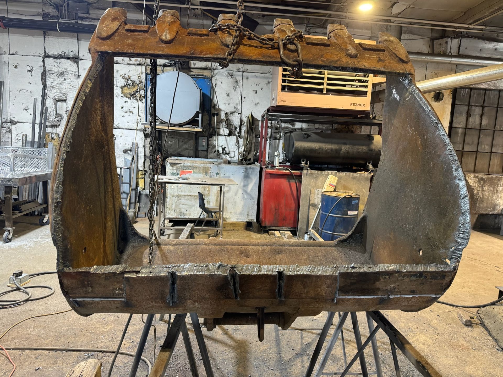 Rusty industrial metal bin or grapple bucket in a workshop, with tools and machinery in the background