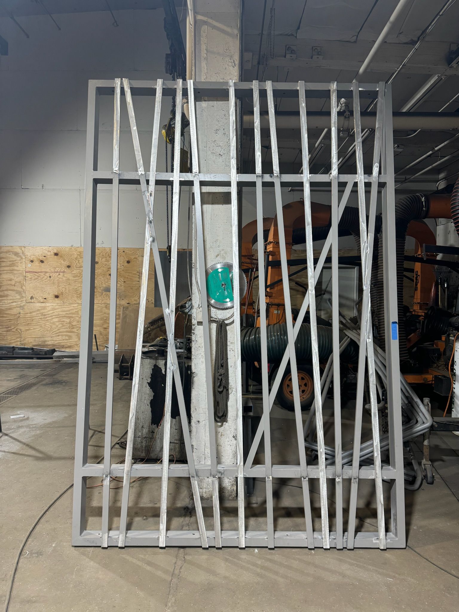 White metal gate leaned against a wall in a garage, with tools and vehicles visible behind it.