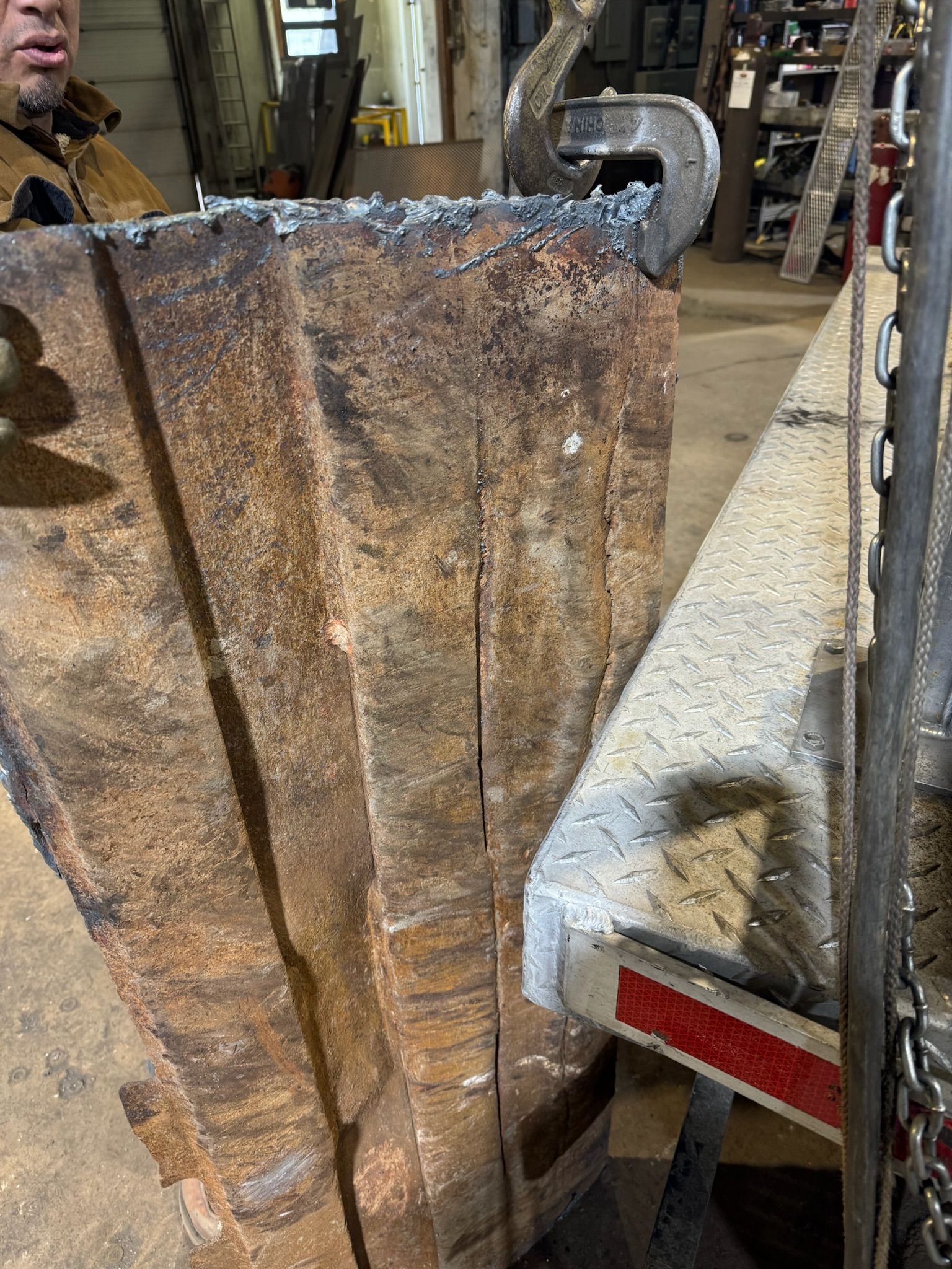 Rusty metal panel beside a truck in a workshop, with equipment and tools in the background.