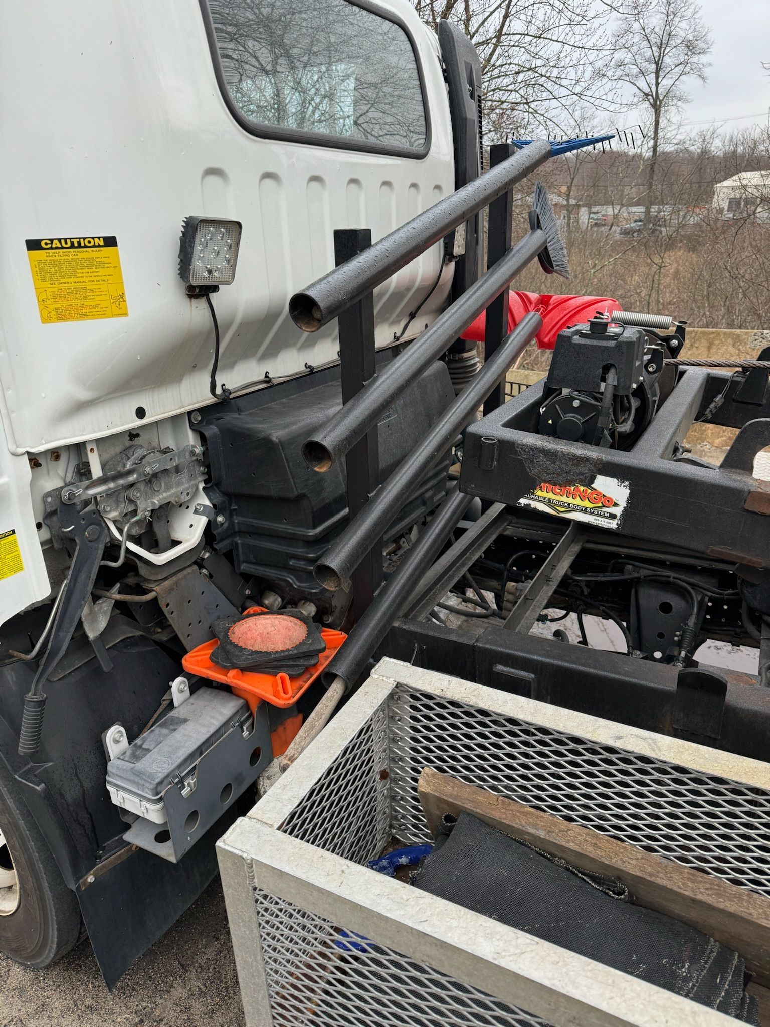 Truck-mounted equipment with black rails and orange components beside a white vehicle