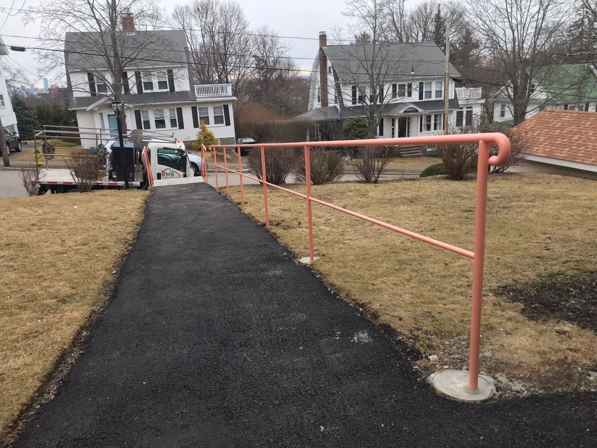Accessible walkway with a red handrail leading through a grassy park toward houses and a playground