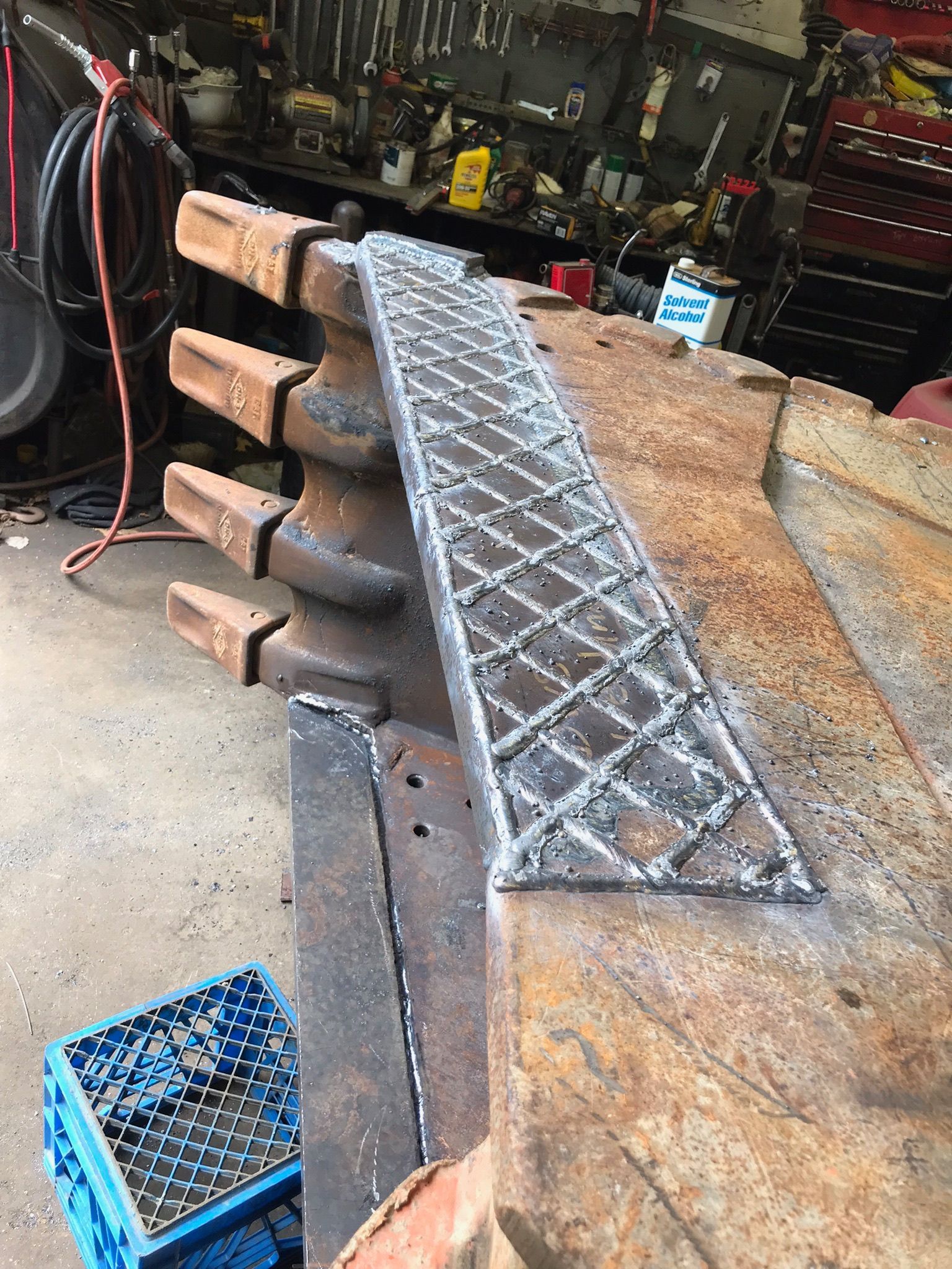 Workshop with a metal diamond-plate ramp laid across stacked timber beams and a rusty steel surface.