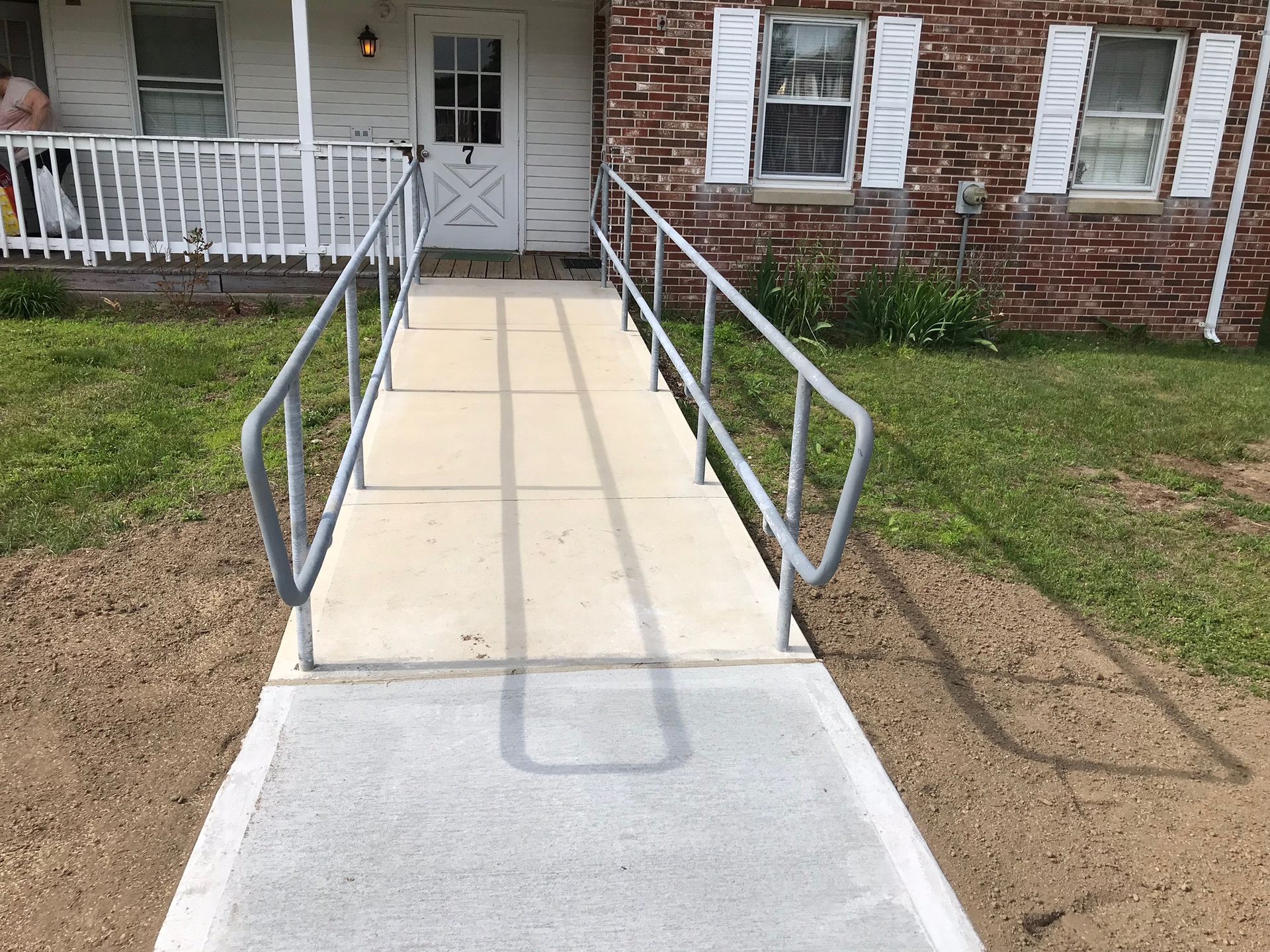 Concrete ramp with metal railings leading to a front porch entrance of a house.