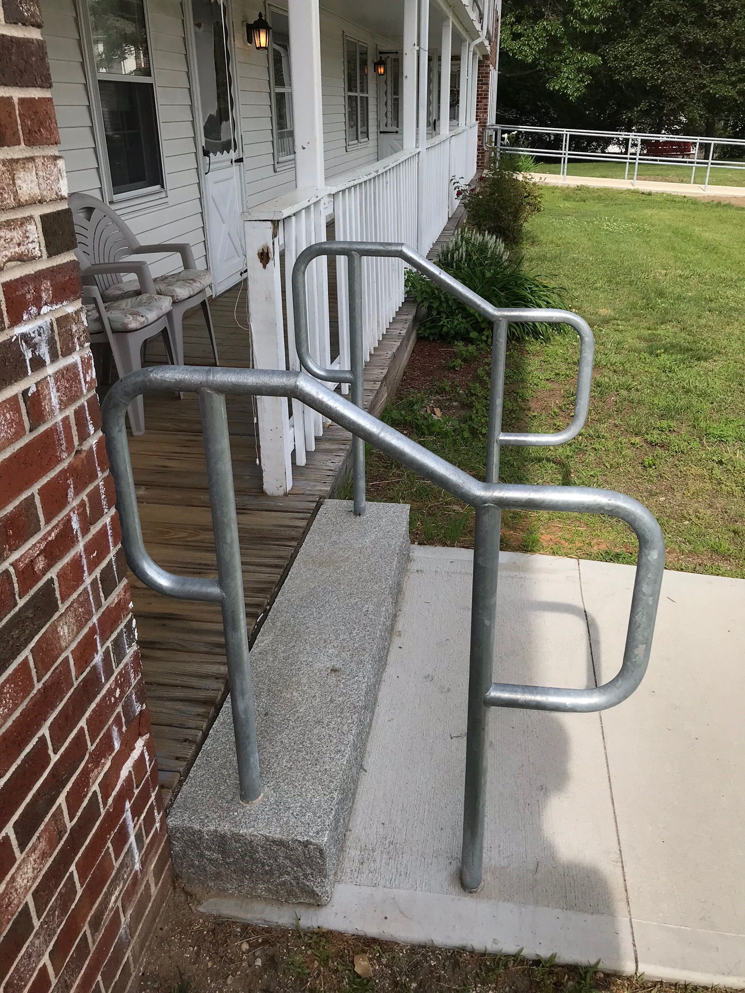 Accessible ramp and handrails beside a brick building entrance, with concrete steps and sidewalk.